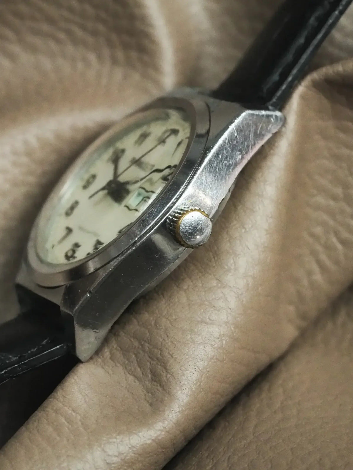 Vintage Omega watch with silver case, cream dial, black leather strap on textured fabric