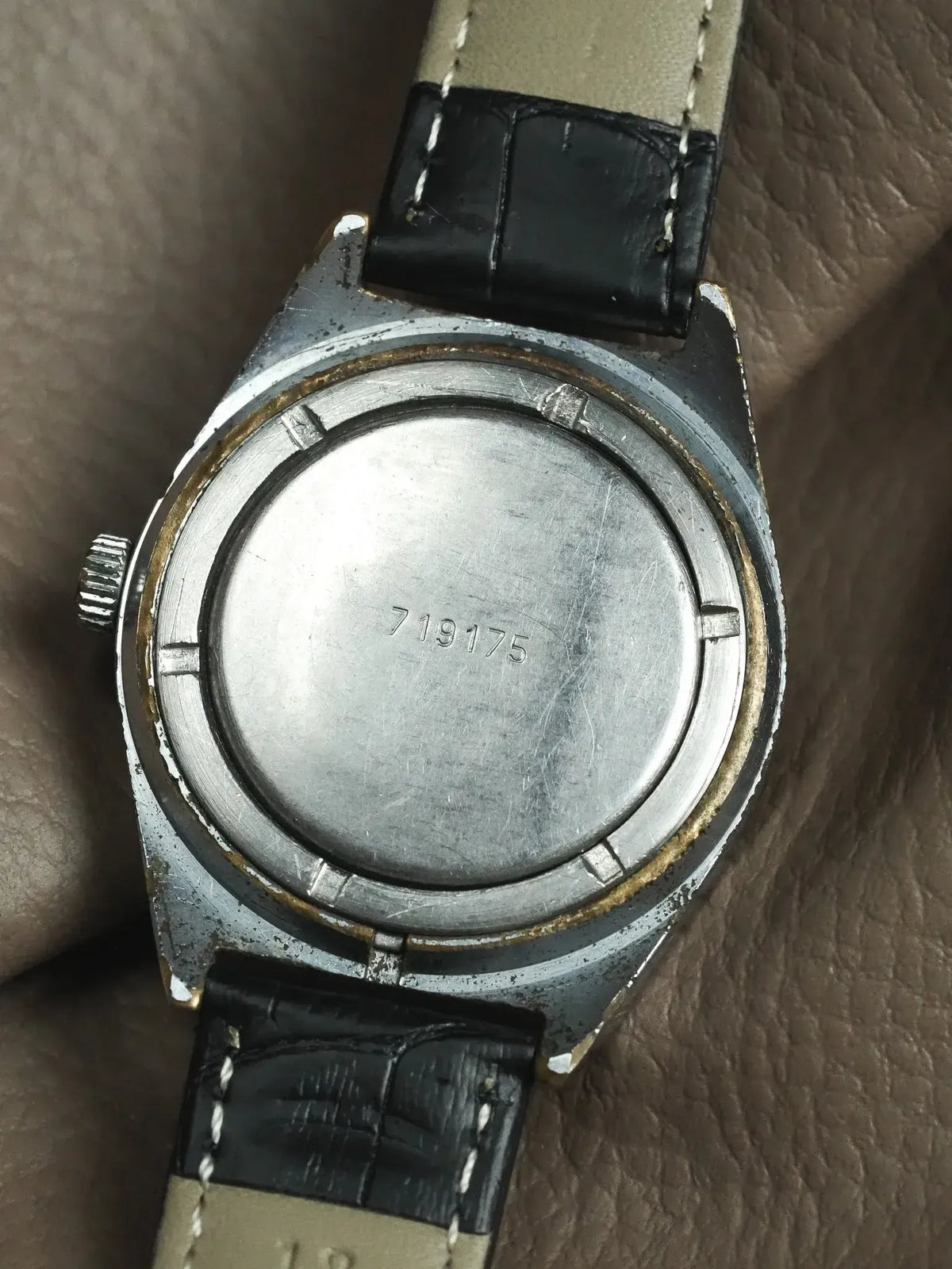 Vintage watch with engraved case back, black leather strap, and visible serial number