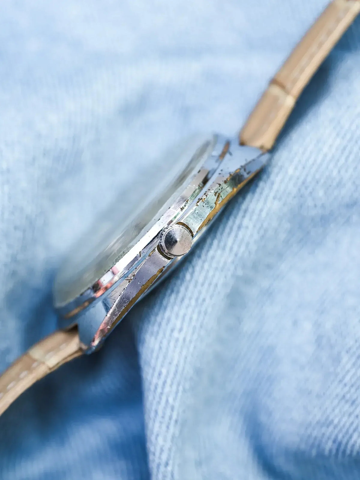Vintage watch side view showing worn gold-toned case and crown on blue fabric