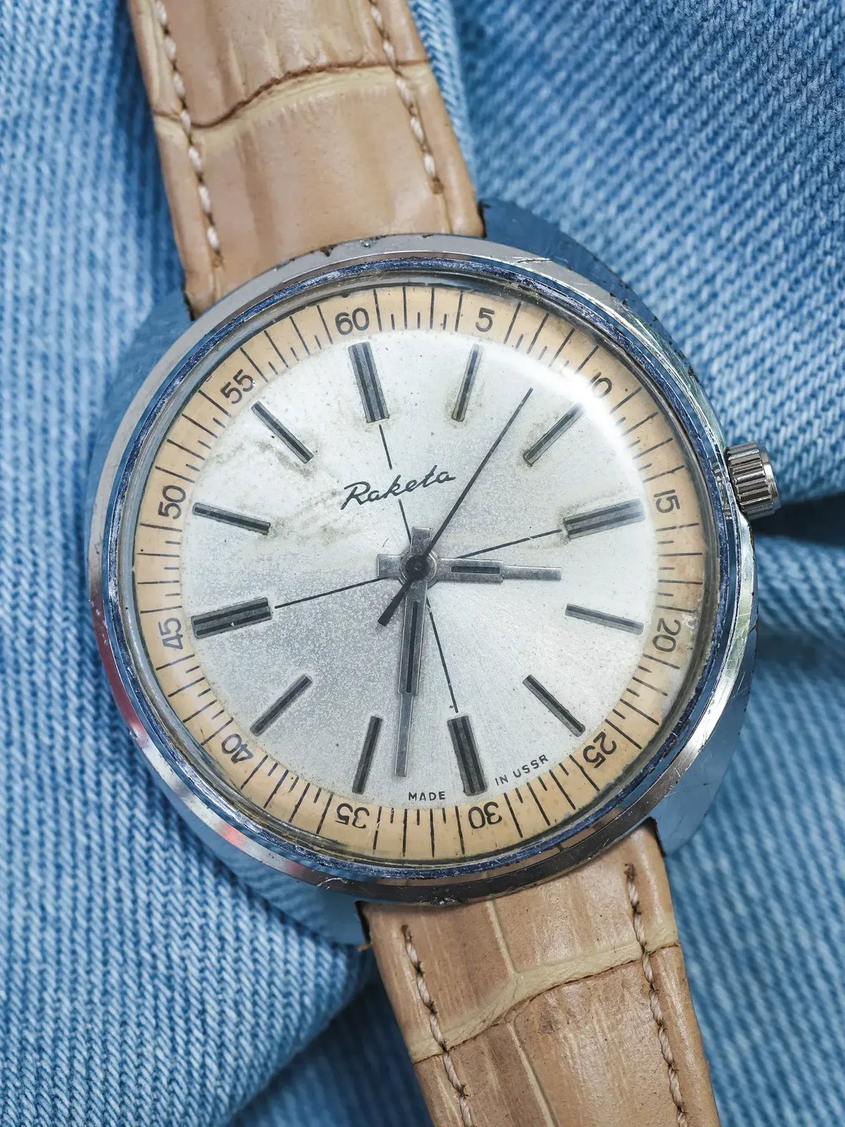 Raketa vintage watch with silver dial, tan leather strap, on denim background