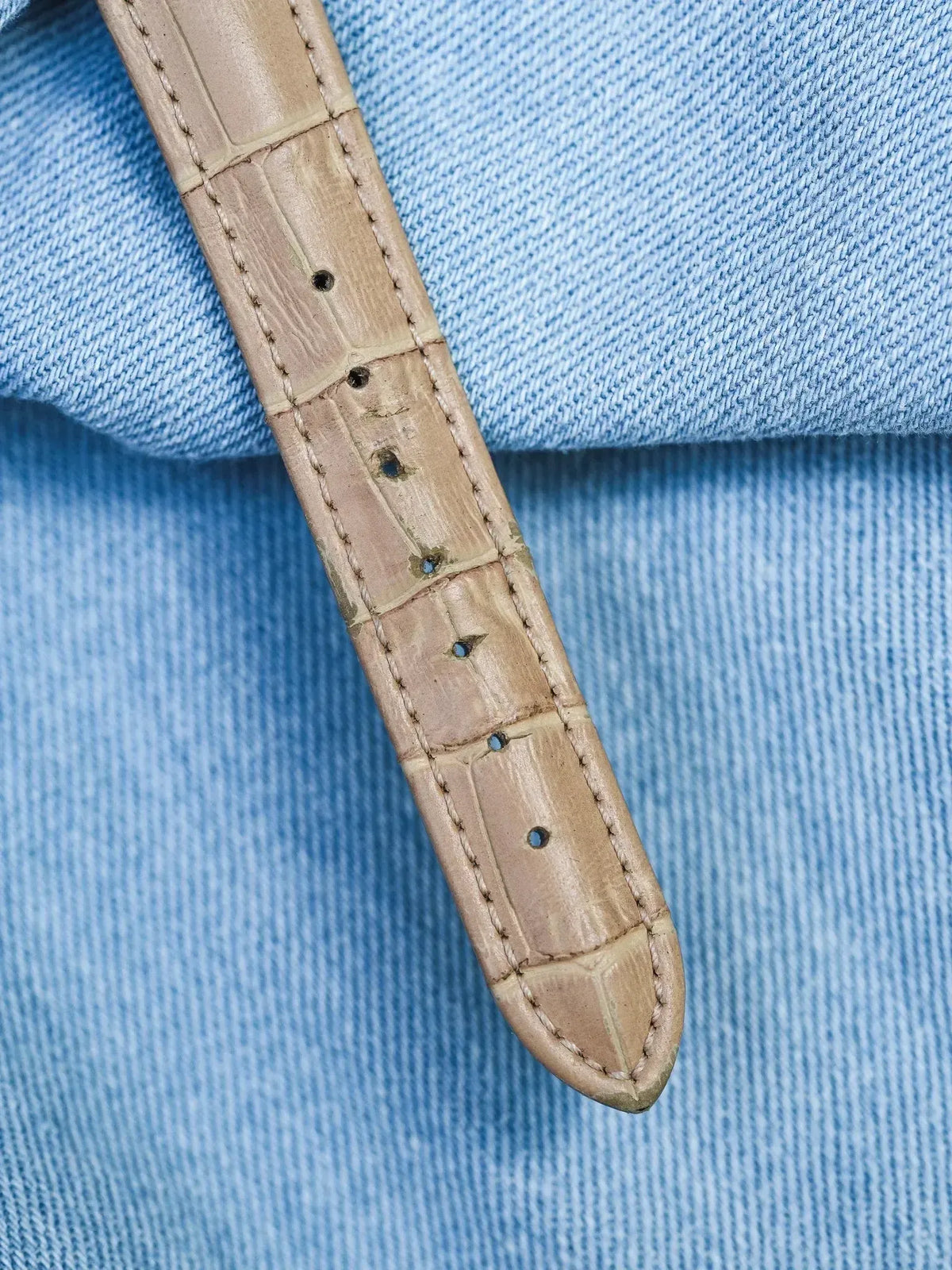 Beige alligator leather watch strap with visible stitching on blue denim background