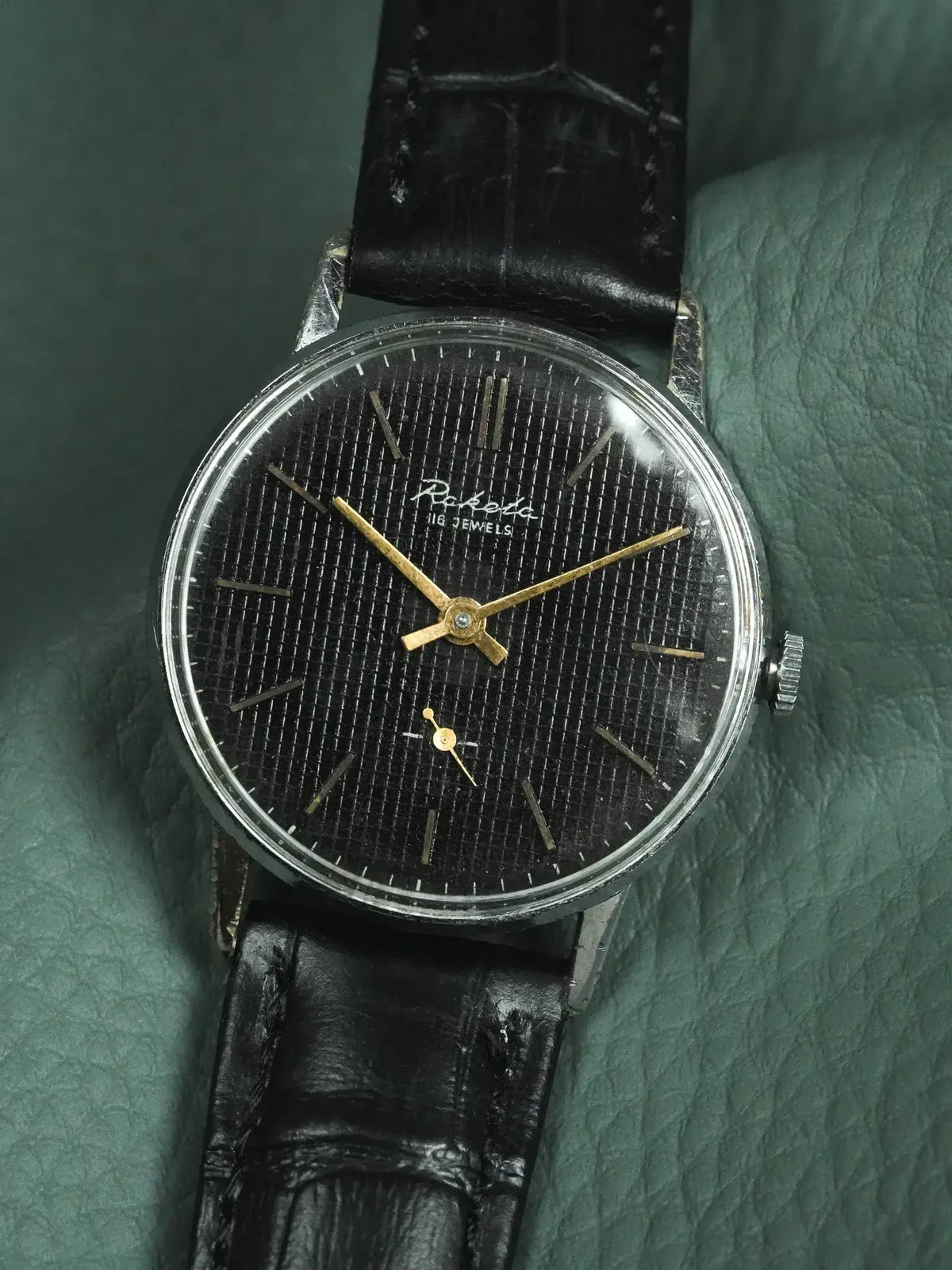 Raketa vintage watch with black textured dial, gold hands, and black leather strap