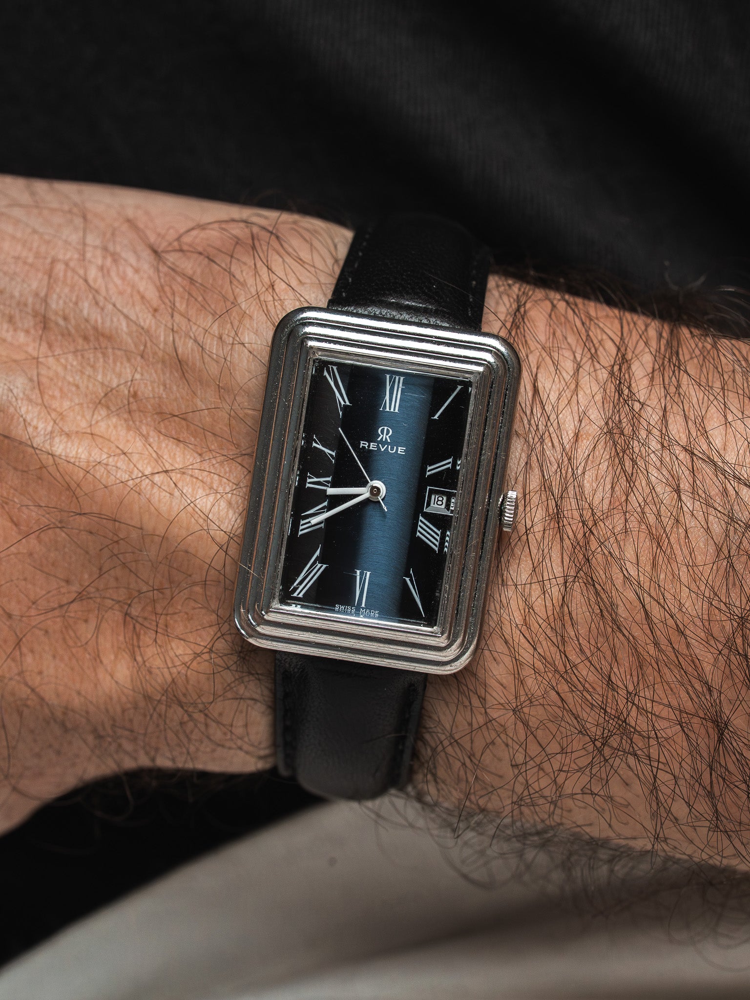 Revue vintage rectangular watch with black dial, Roman numerals, leather strap on wrist