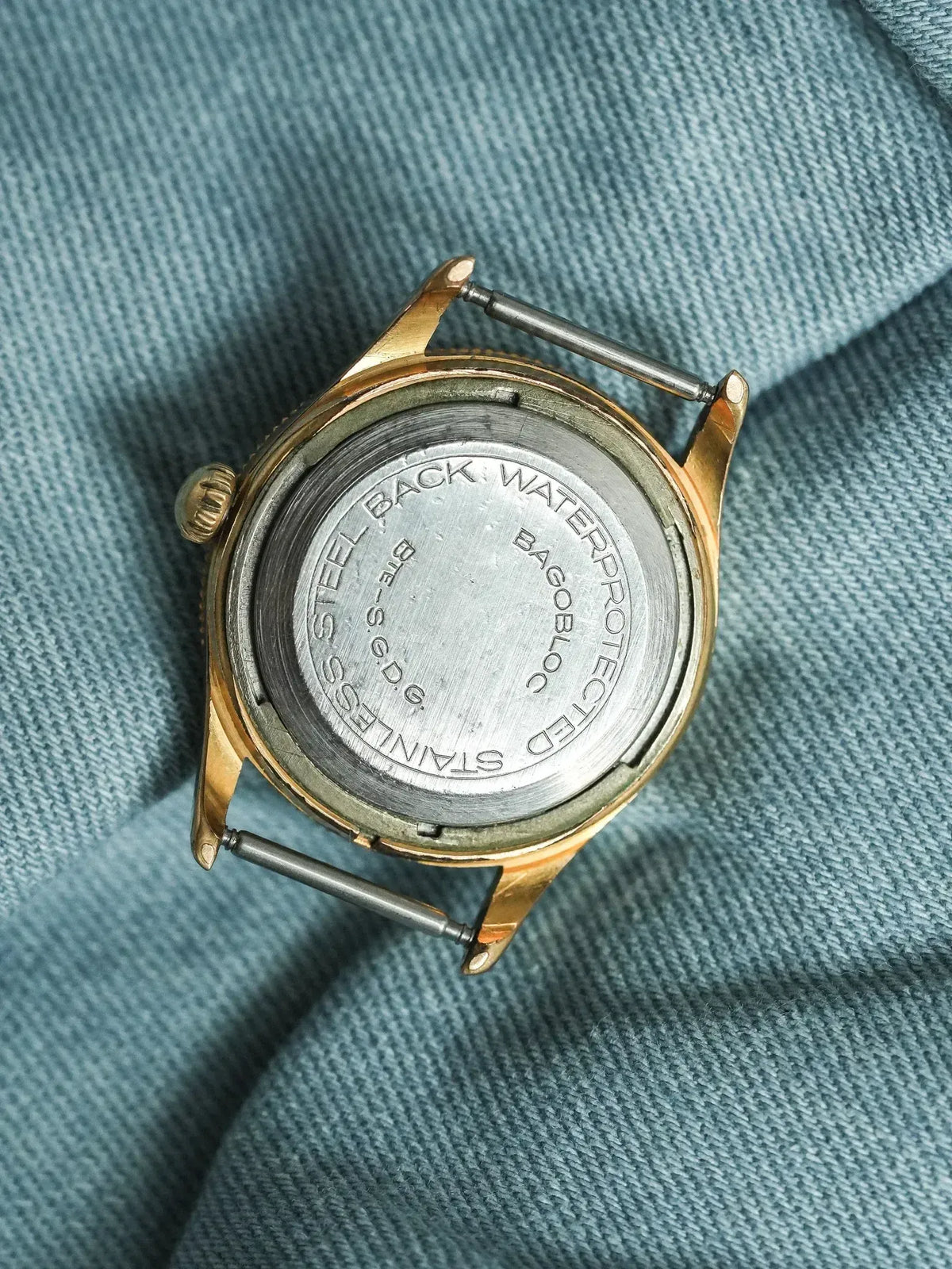 Vintage BAGOBLOC watch with stainless steel back, gold case, resting on blue fabric