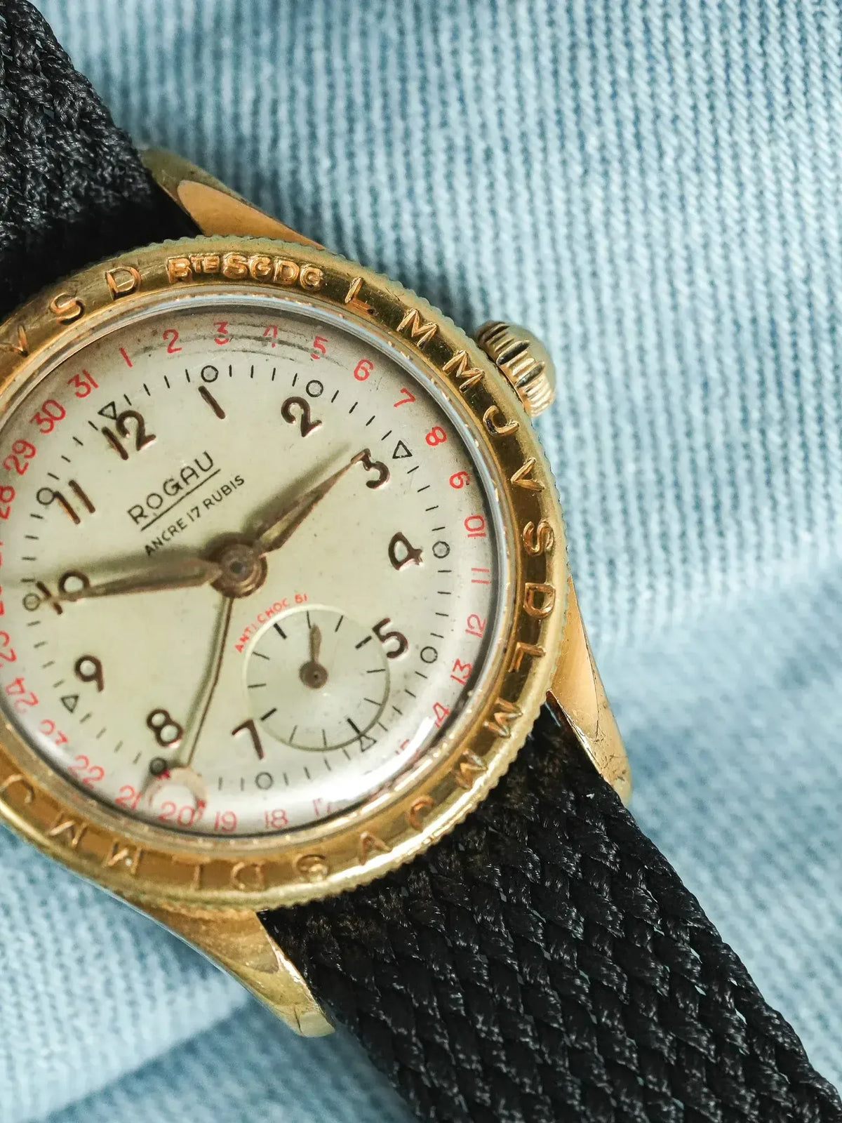 Rogau vintage watch with gold case, cream dial, black fabric strap on denim