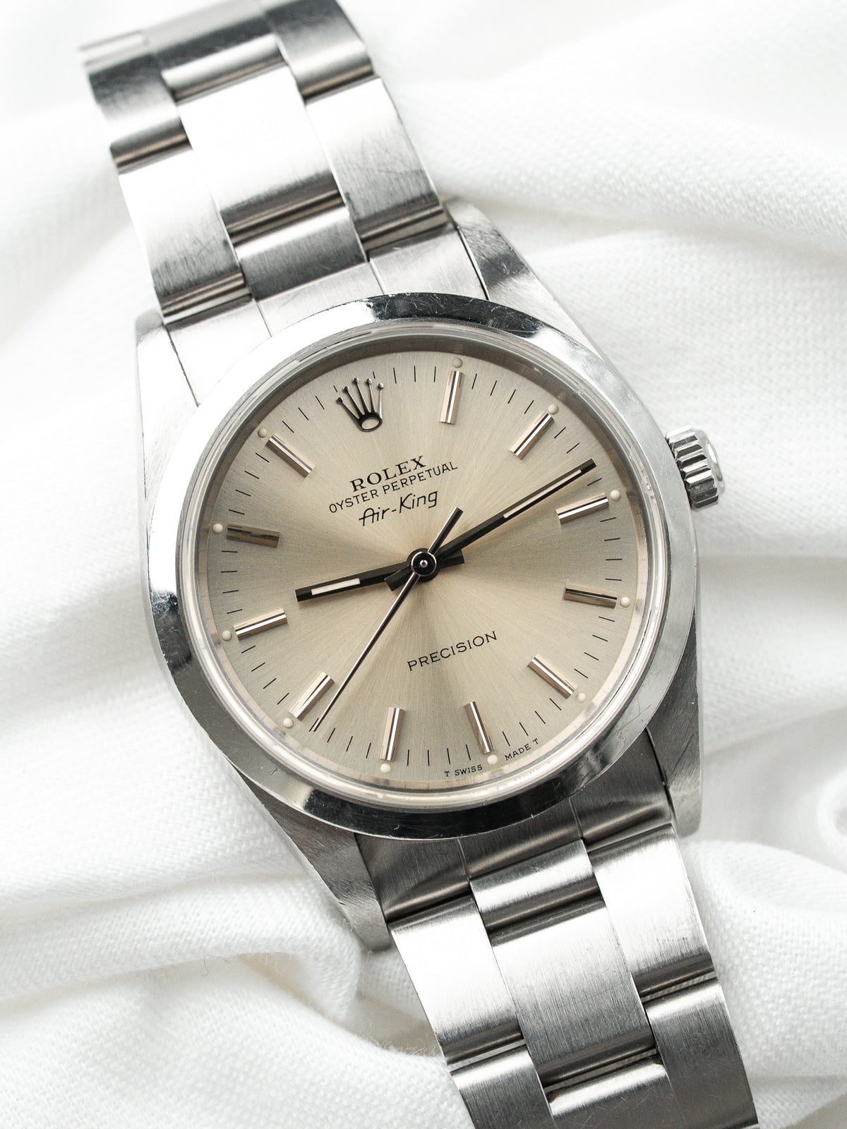 Montre Rolex Air-King vintage en acier, cadran champagne, sur fond de tissu blanc