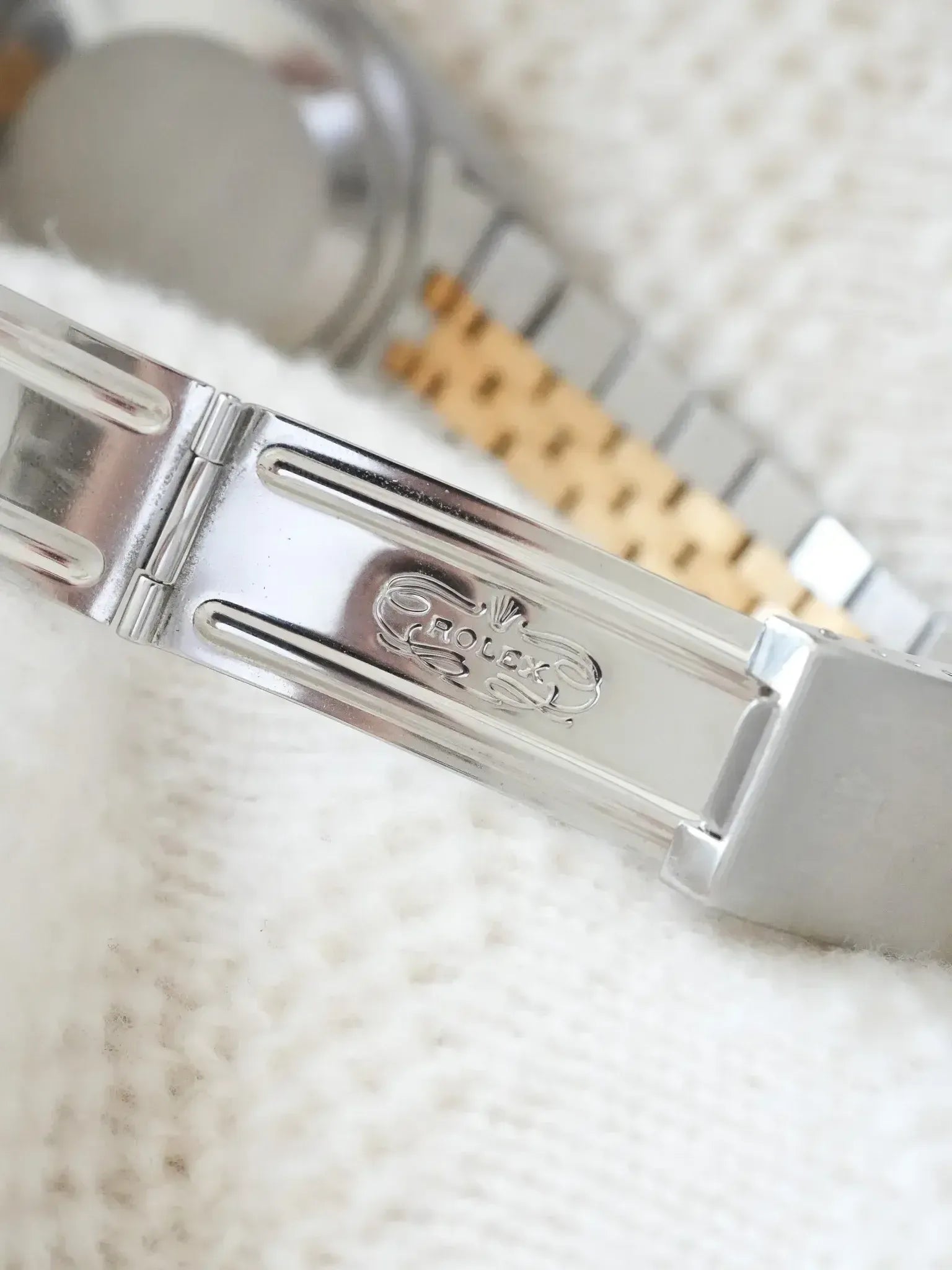 Rolex vintage watch clasp with engraved logo, stainless steel and gold bracelet on textured white background