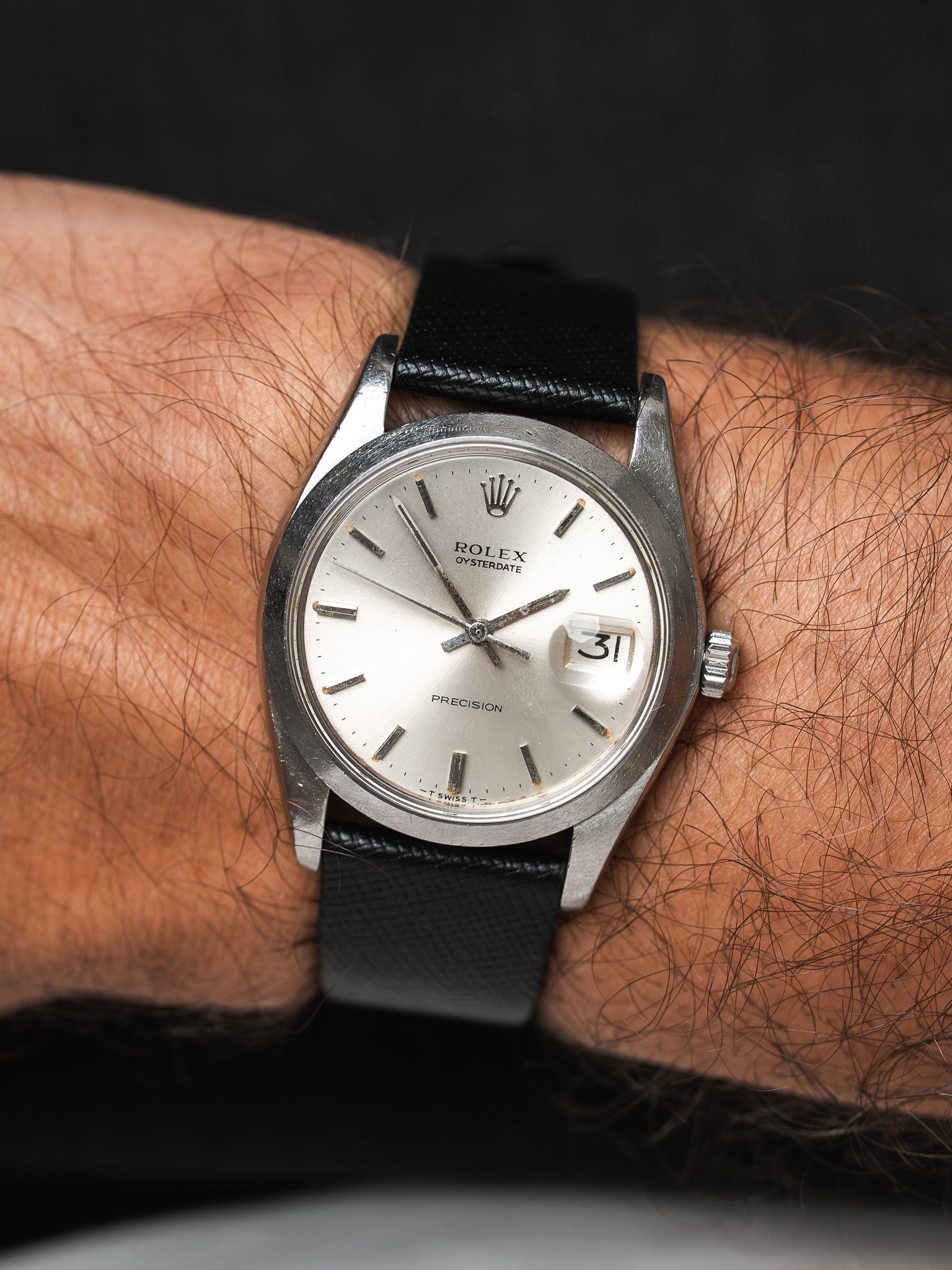 Rolex Oysterdate vintage watch with silver dial and black leather strap on wrist