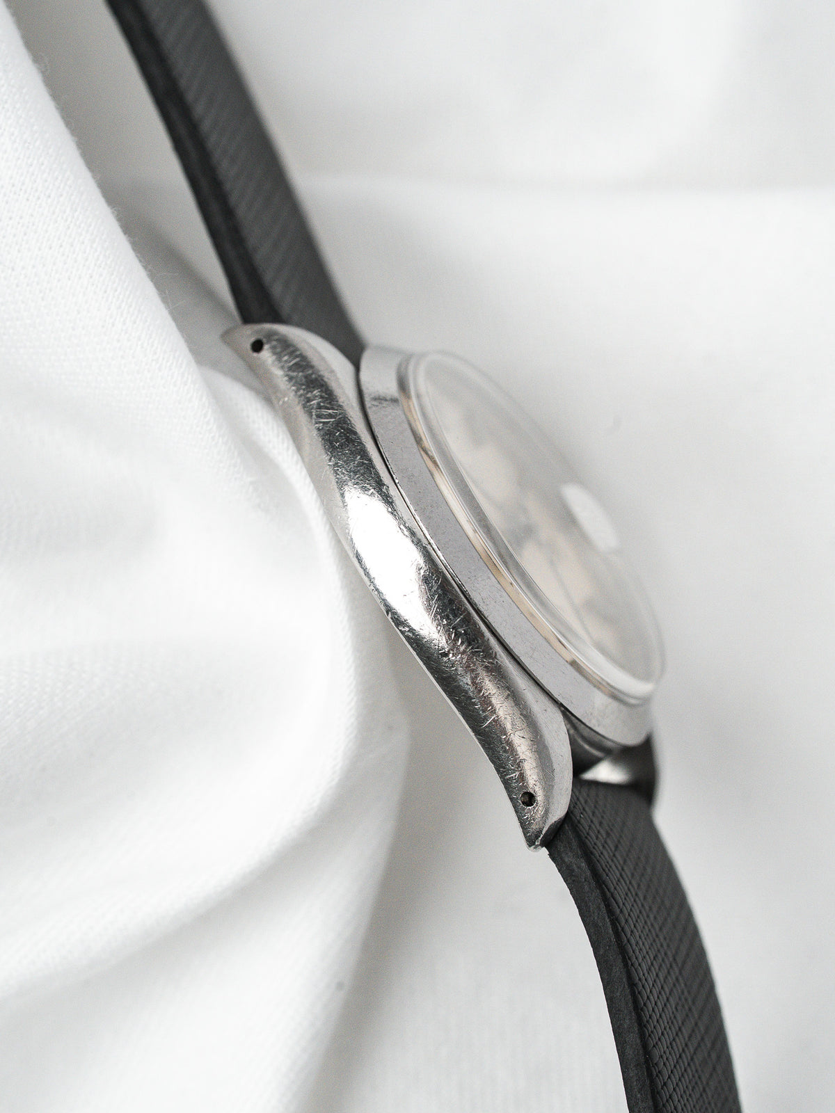 Vintage Omega watch with steel case and black leather strap on white fabric