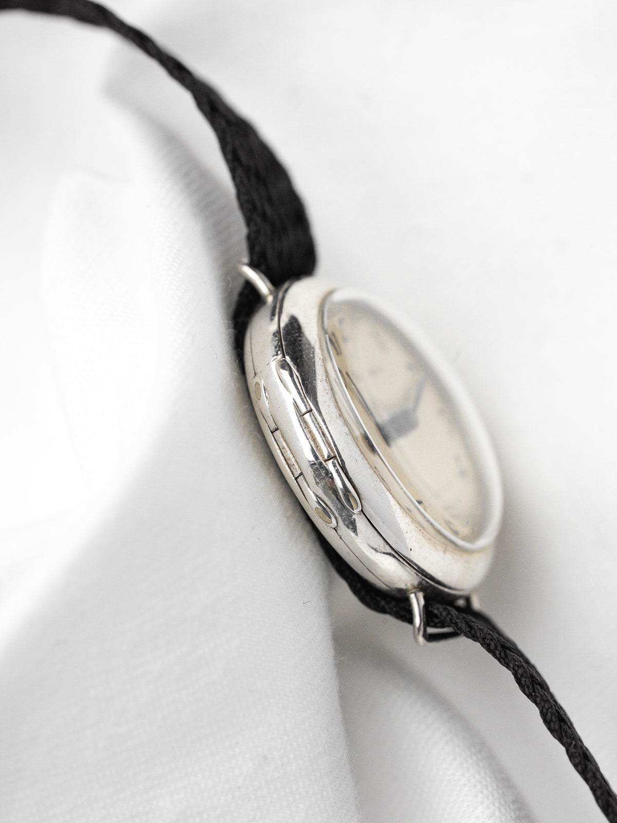 Montre vintage au boîtier argenté et bracelet en cordon noir sur fond blanc