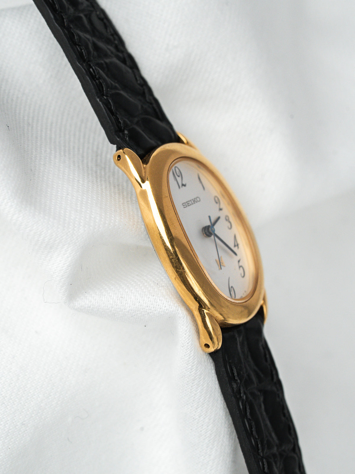 Montre Seiko vintage, boîtier ovale doré, cadran blanc et bracelet cuir noir
