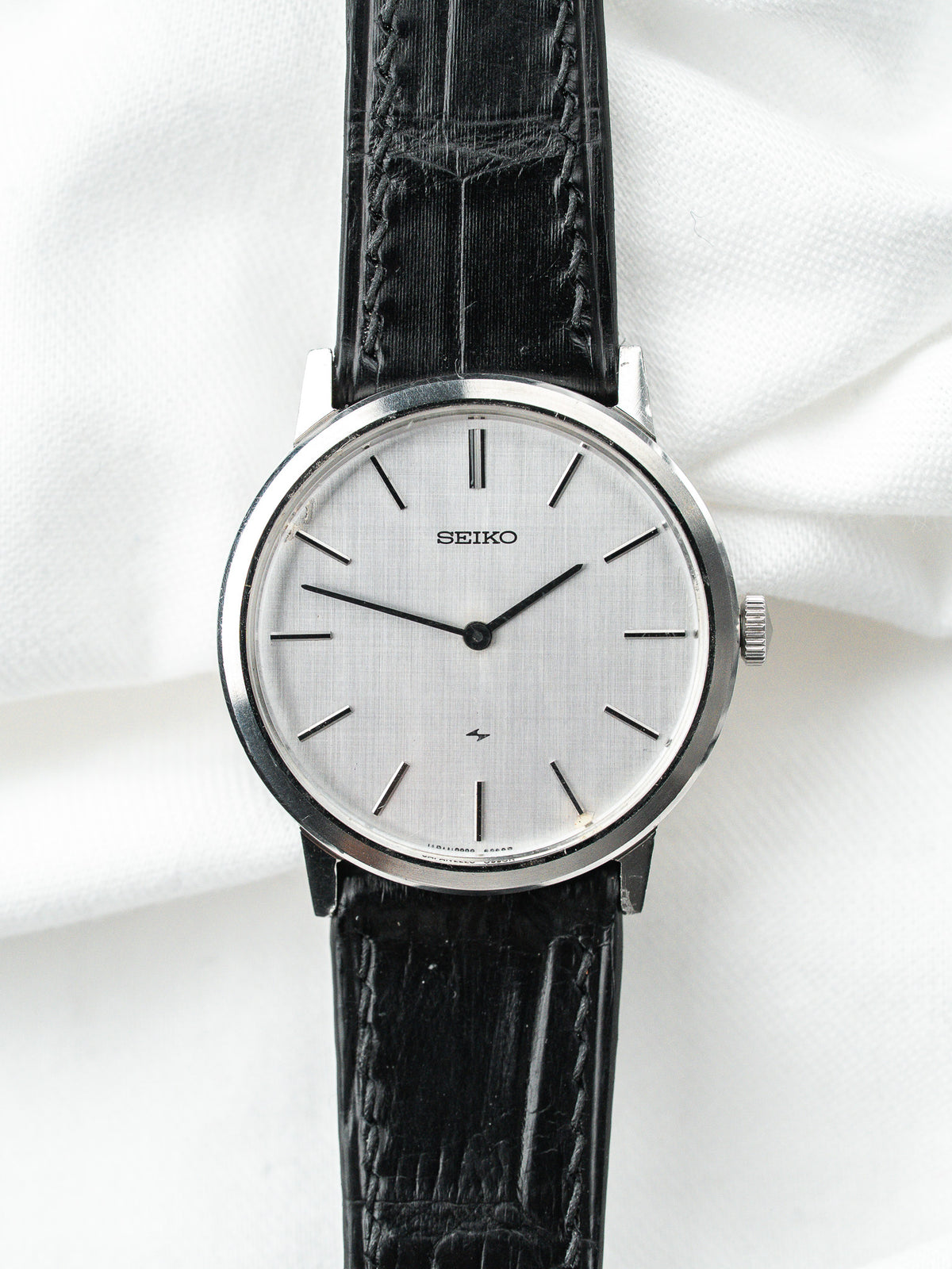 Montre Seiko vintage au cadran argenté et bracelet en cuir noir texturé.