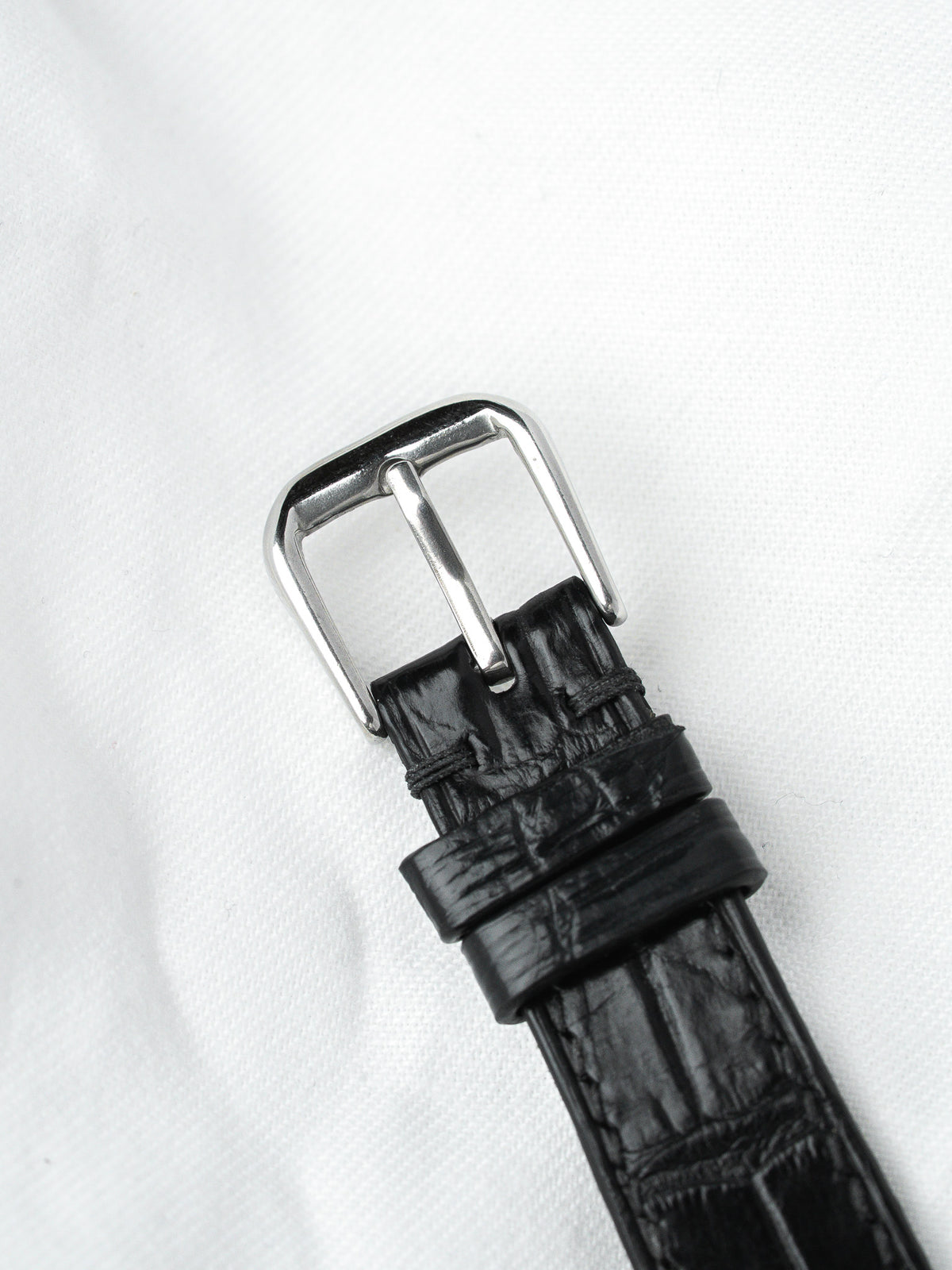 Black alligator leather watch strap with polished steel buckle on white background