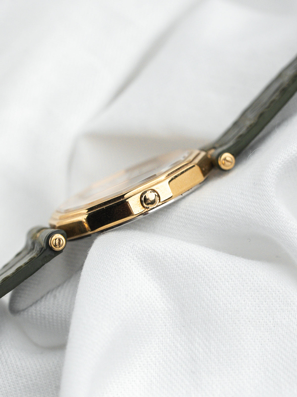 Vue de profil d'une montre vintage au boîtier doré et bracelet en cuir vert.