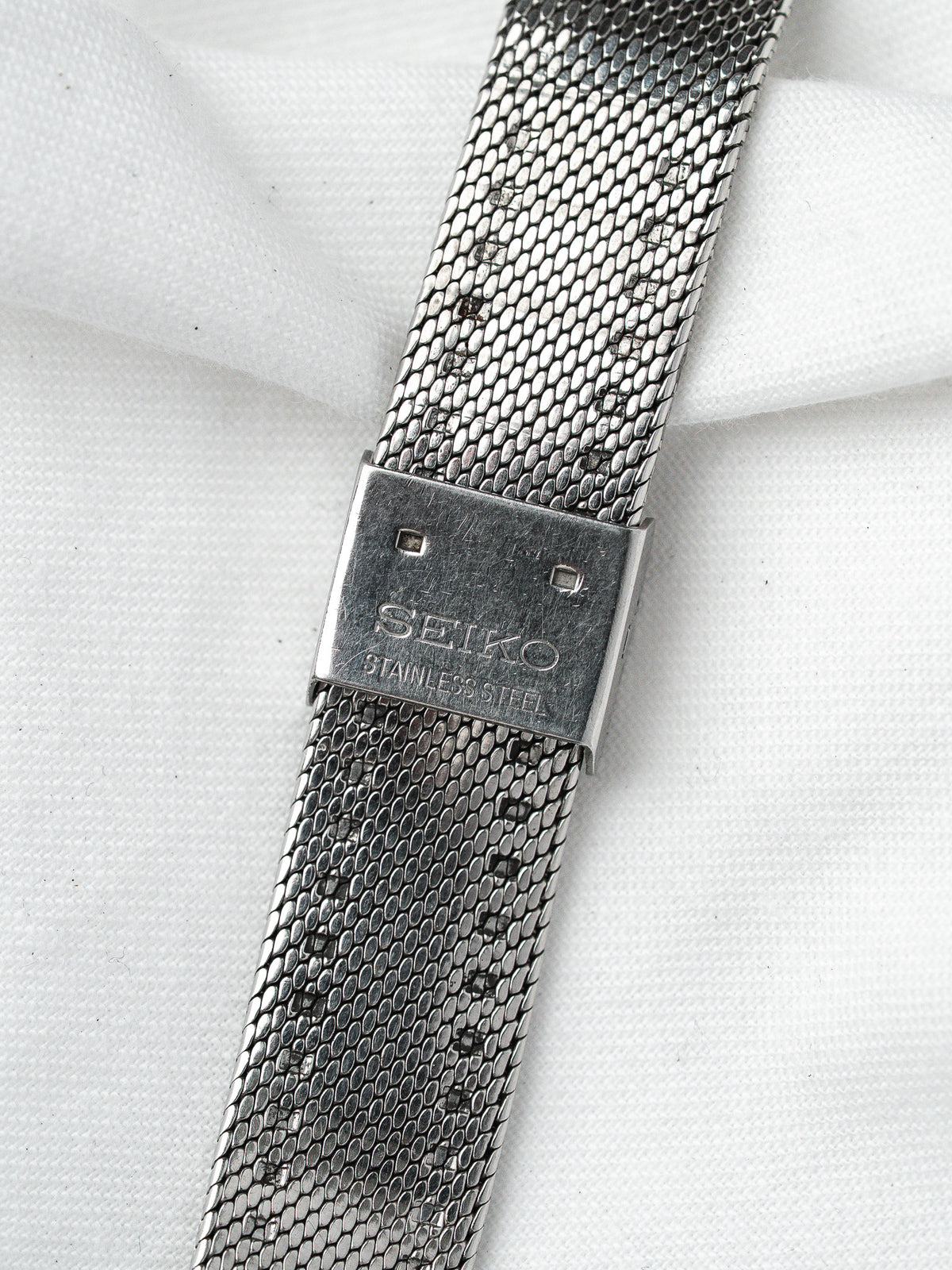Seiko stainless steel mesh bracelet with engraved clasp on white fabric