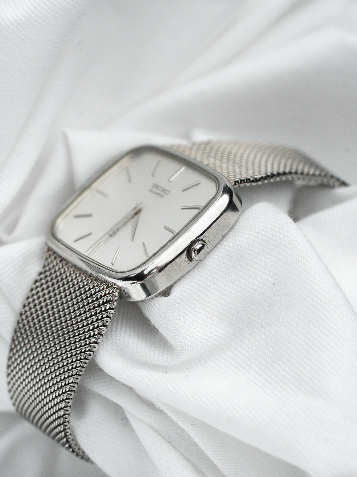 Montre Seiko vintage en acier, boîtier rectangulaire, cadran blanc et bracelet milanais