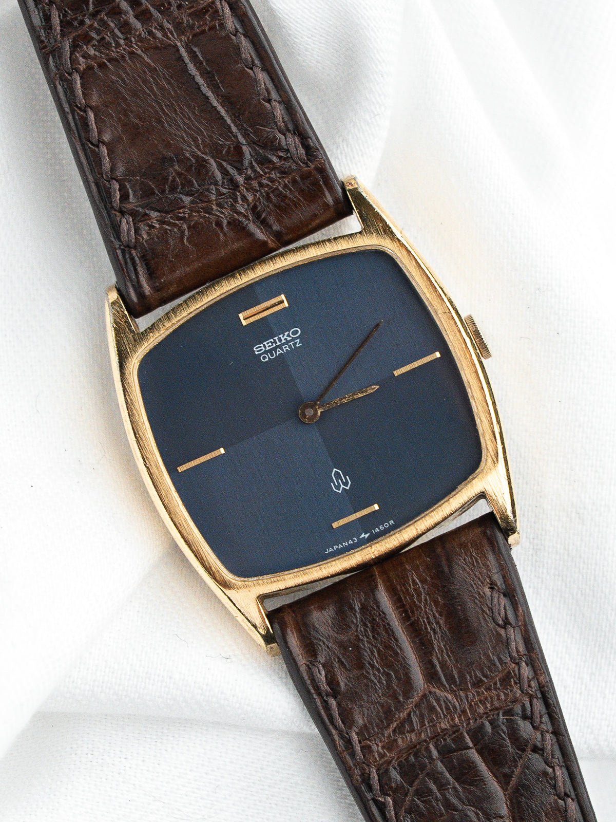 Montre Seiko Quartz vintage au boîtier doré, cadran bleu et bracelet en cuir marron.