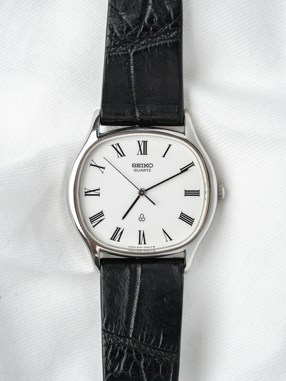 Seiko Quartz vintage watch with white dial, Roman numerals, black leather strap on white background