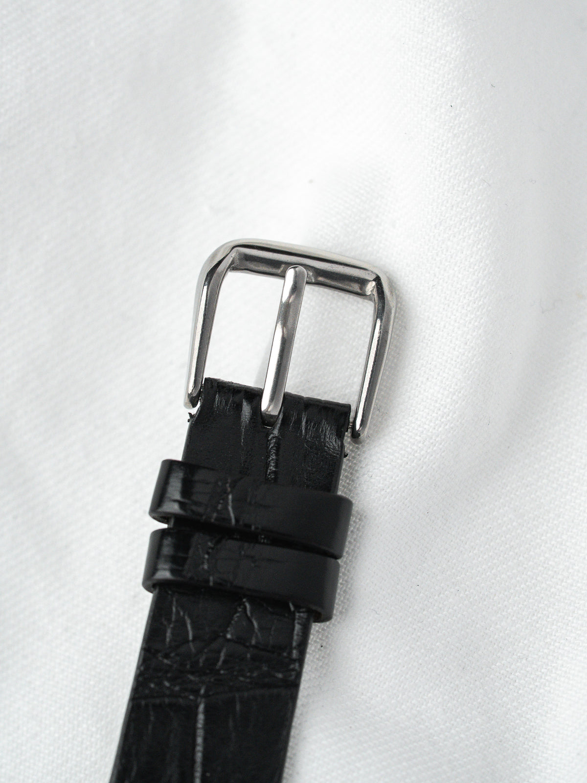 Black alligator leather watch strap with polished steel buckle on white background