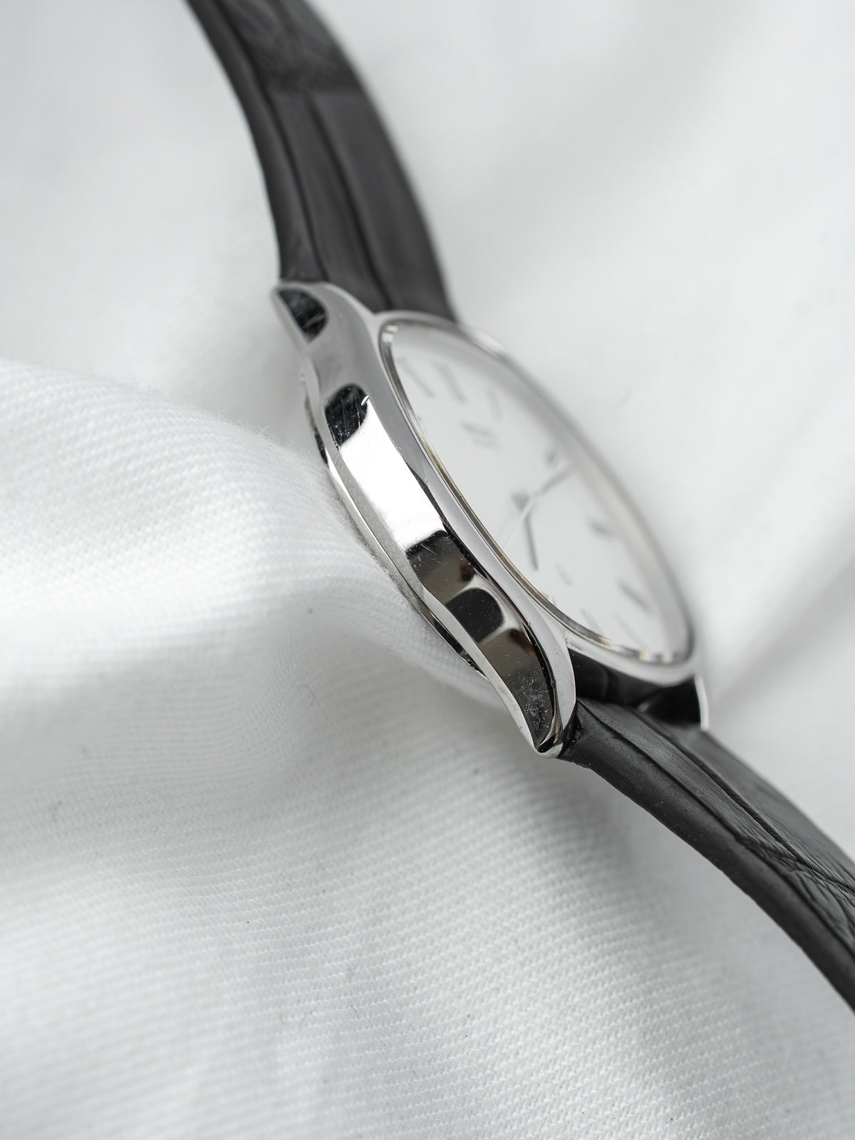 Vintage Cartier watch with silver case, white dial, black leather strap on white fabric