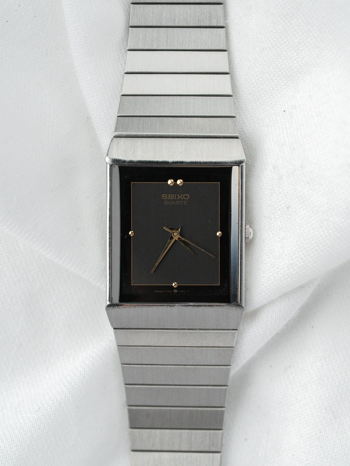 Montre vintage au cadran noir rectangulaire et bracelet en acier argenté.