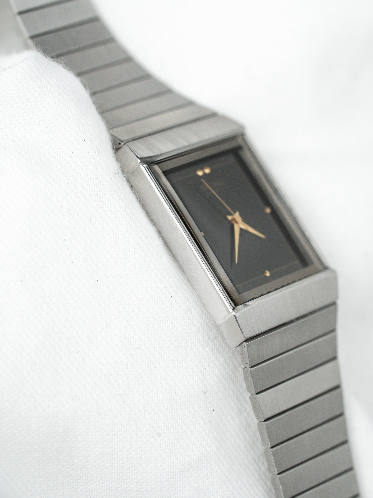 Montre vintage rectangulaire en acier avec cadran noir et bracelet à maillons argentés.