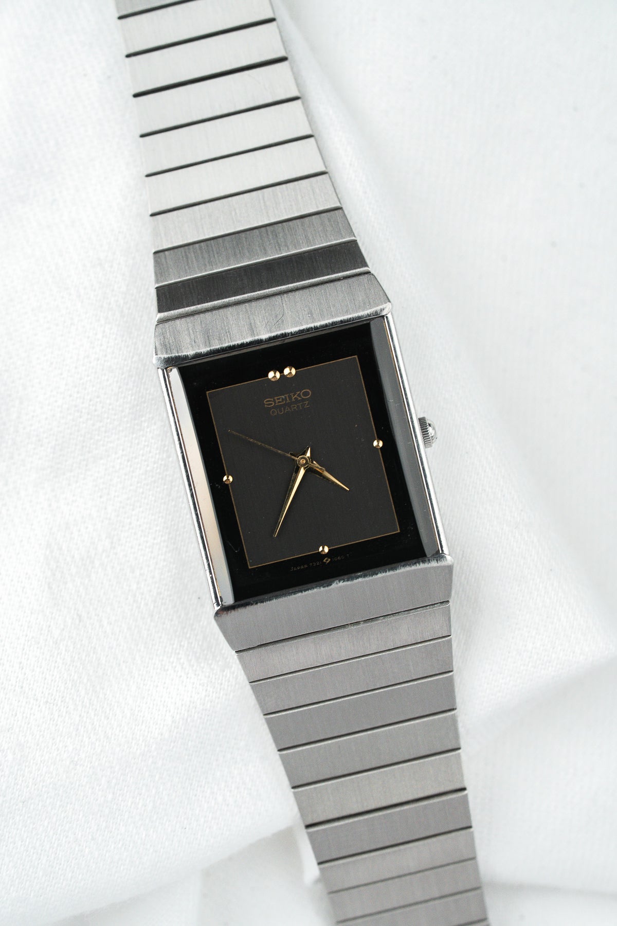 Montre Seiko Quartz vintage avec cadran rectangulaire noir et bracelet en acier argenté.