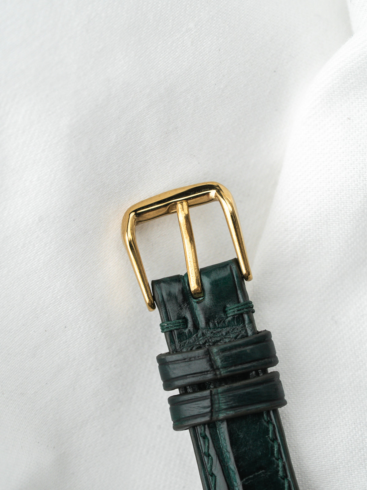 Boucle de bracelet de montre en or avec cuir vert foncé sur fond blanc