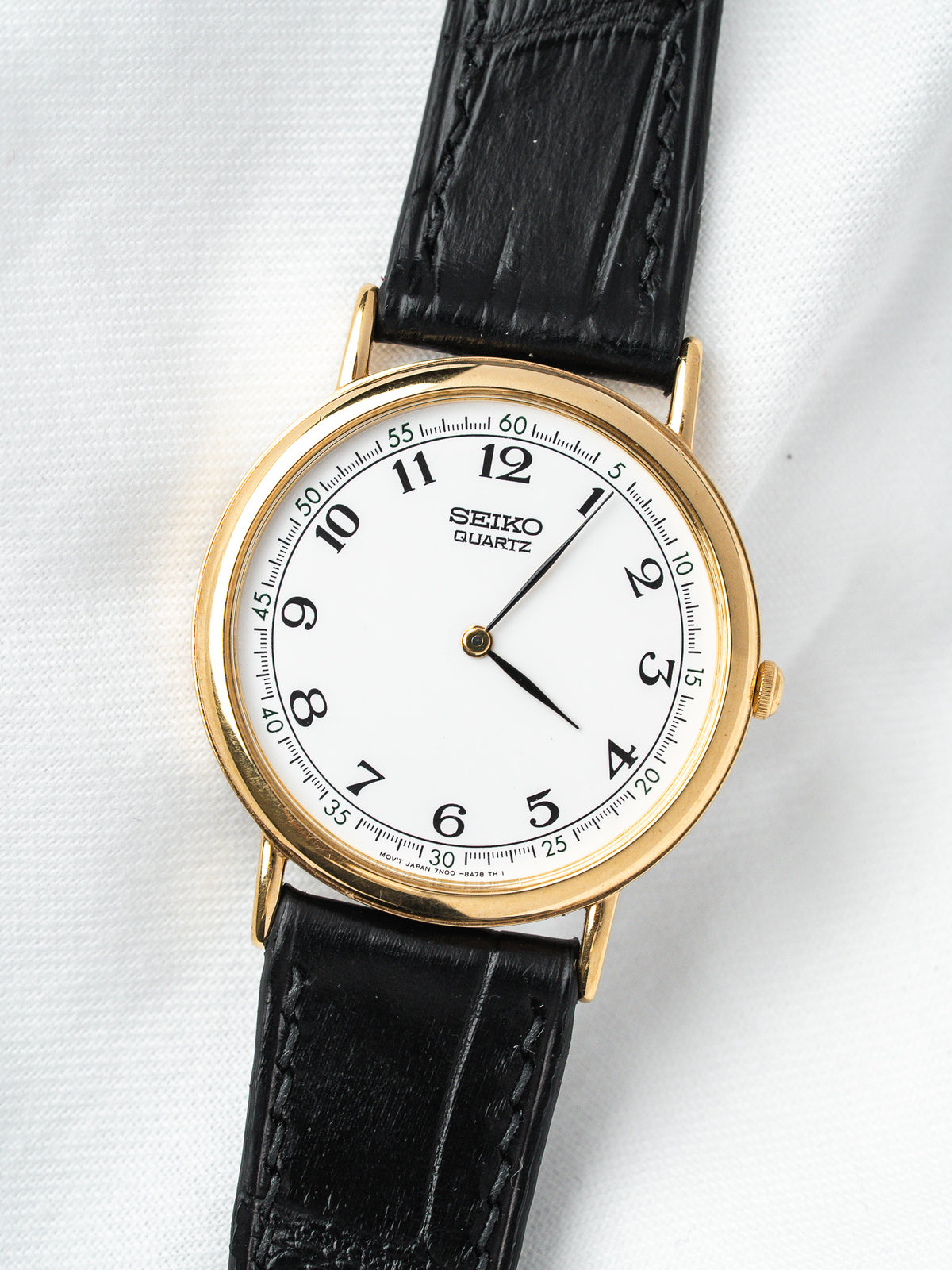 Seiko Quartz vintage watch with gold case, white dial, black leather strap on white background