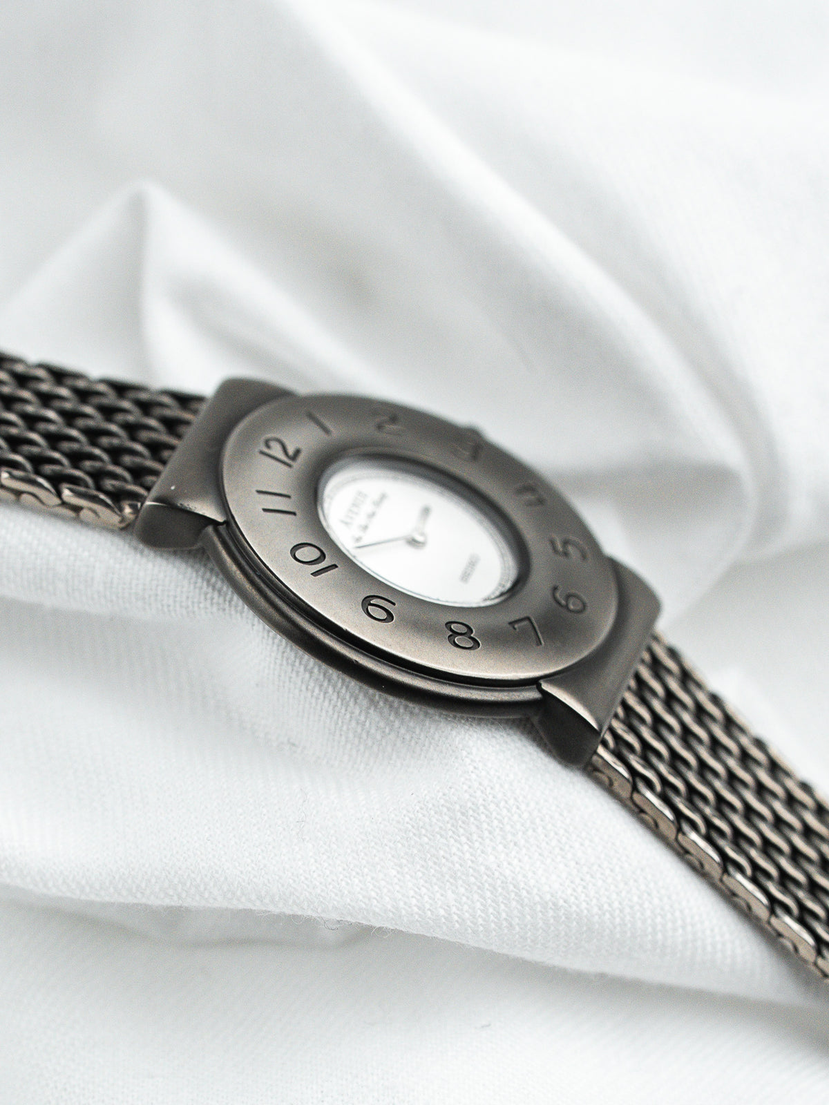 Montre vintage en acier avec bracelet maille milanaise et cadran blanc sur fond blanc