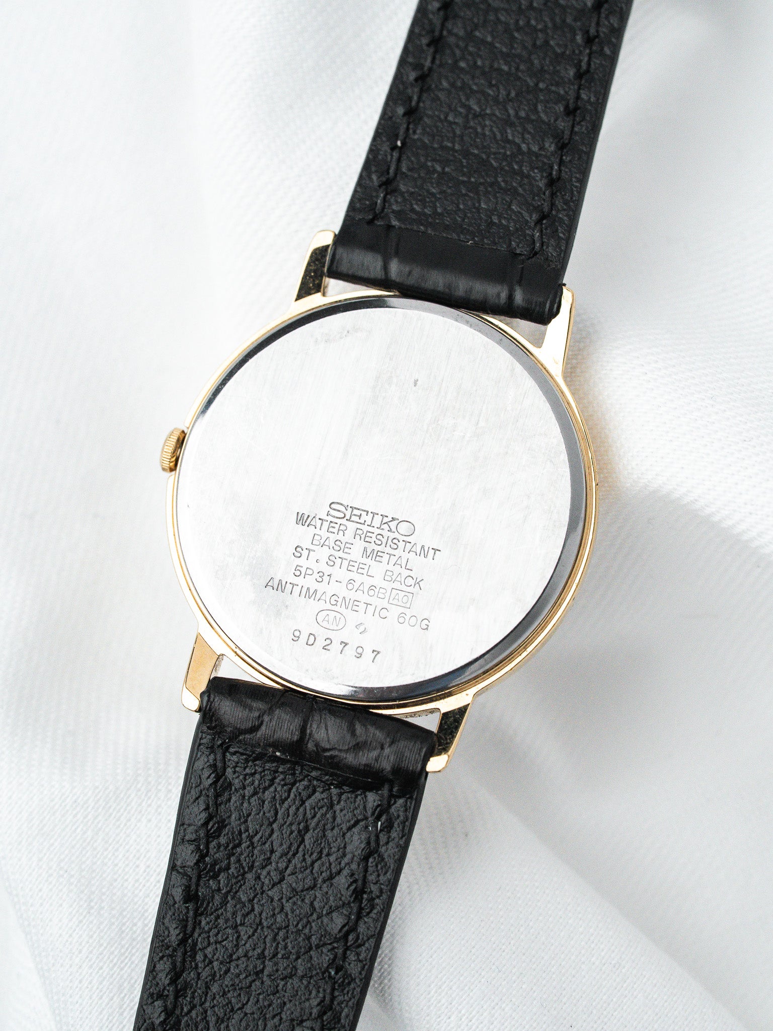 Seiko vintage watch with gold case, black leather strap, steel back engraved details