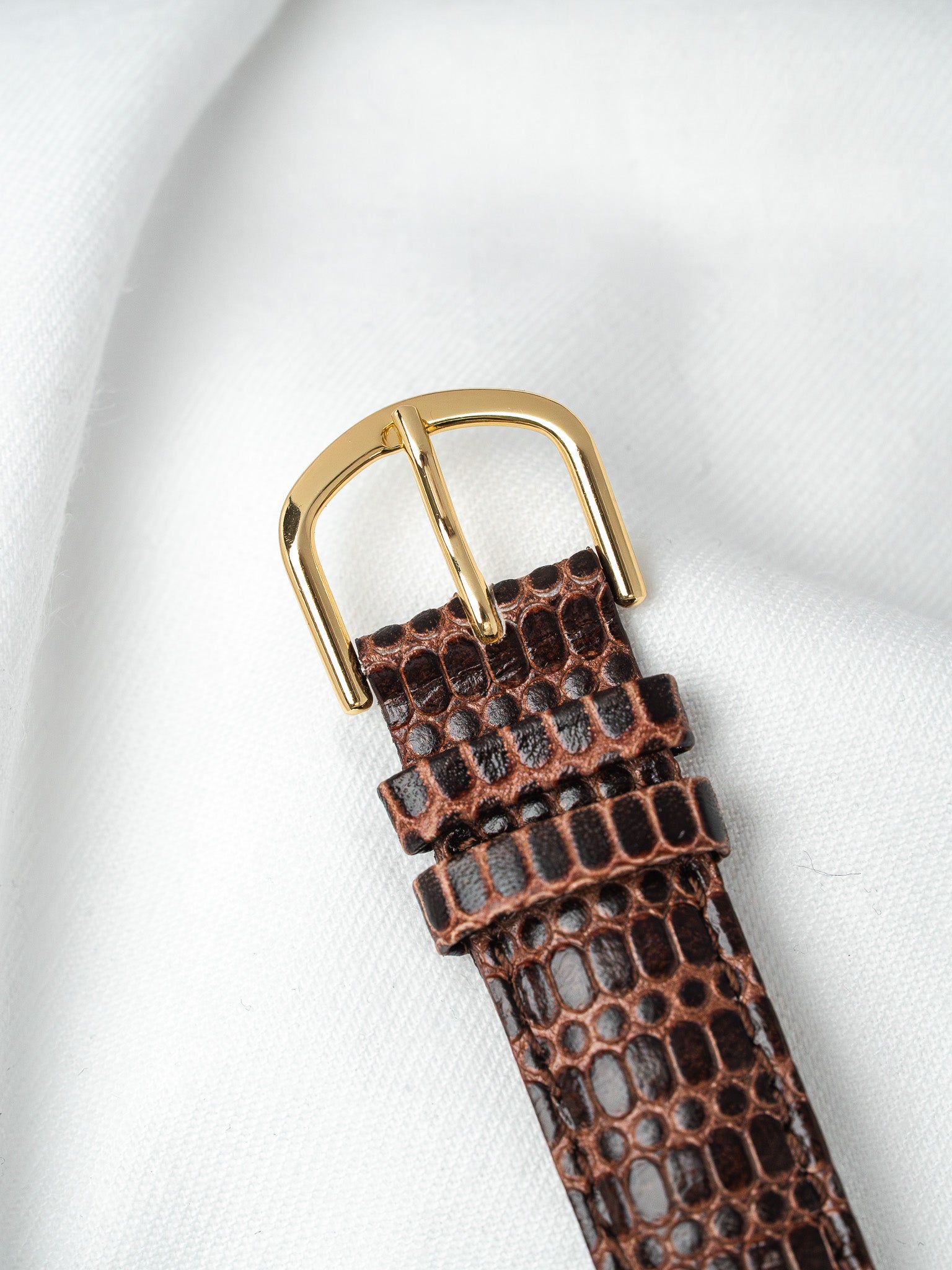 Brown crocodile leather watch strap with gold buckle on white fabric