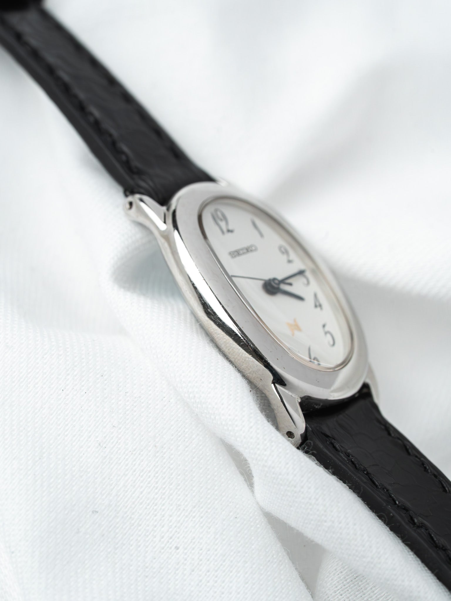 Seiko vintage watch with white dial, black leather strap, silver case on white fabric