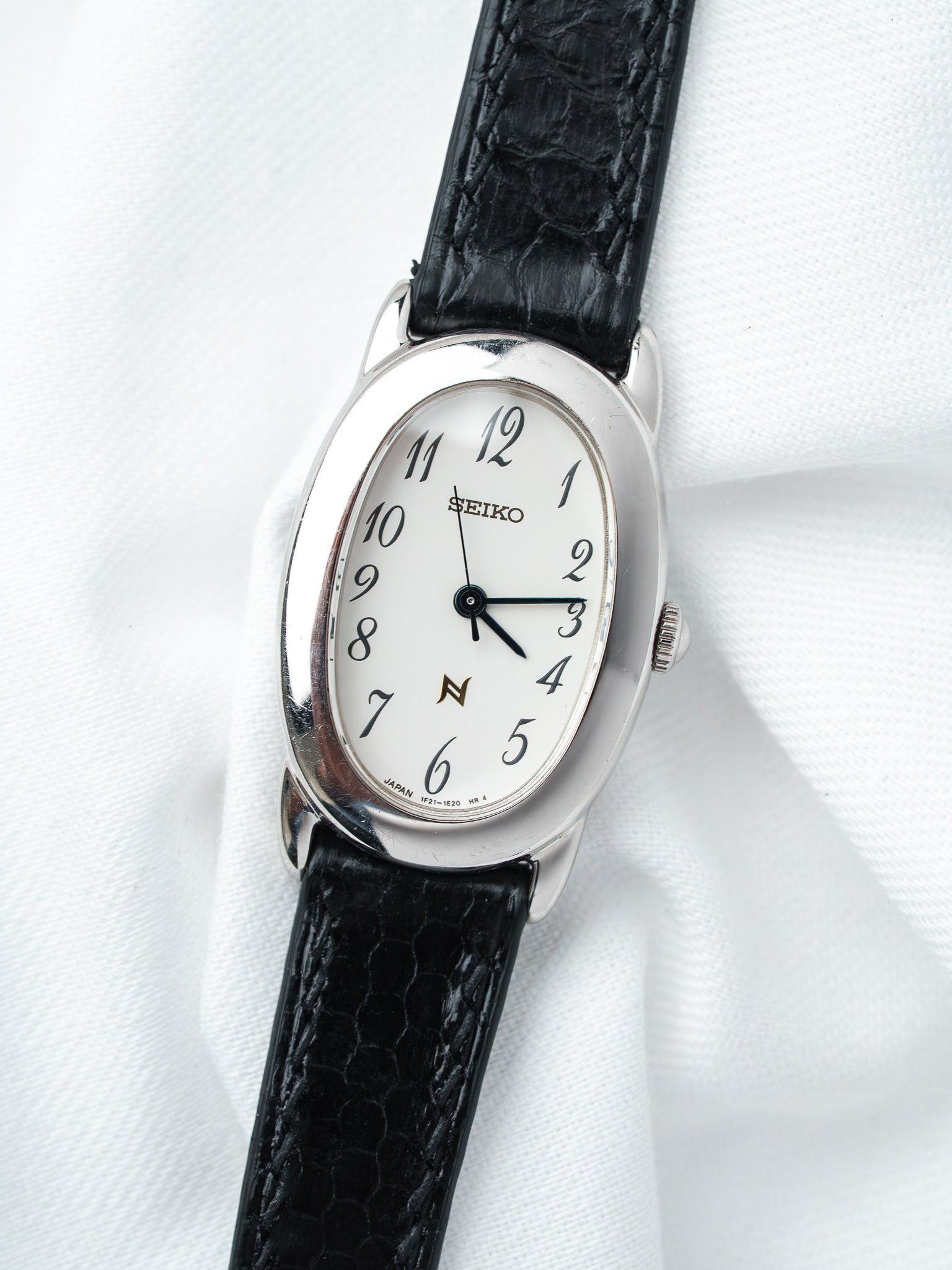 Seiko vintage watch with white dial, black leather strap, on white fabric