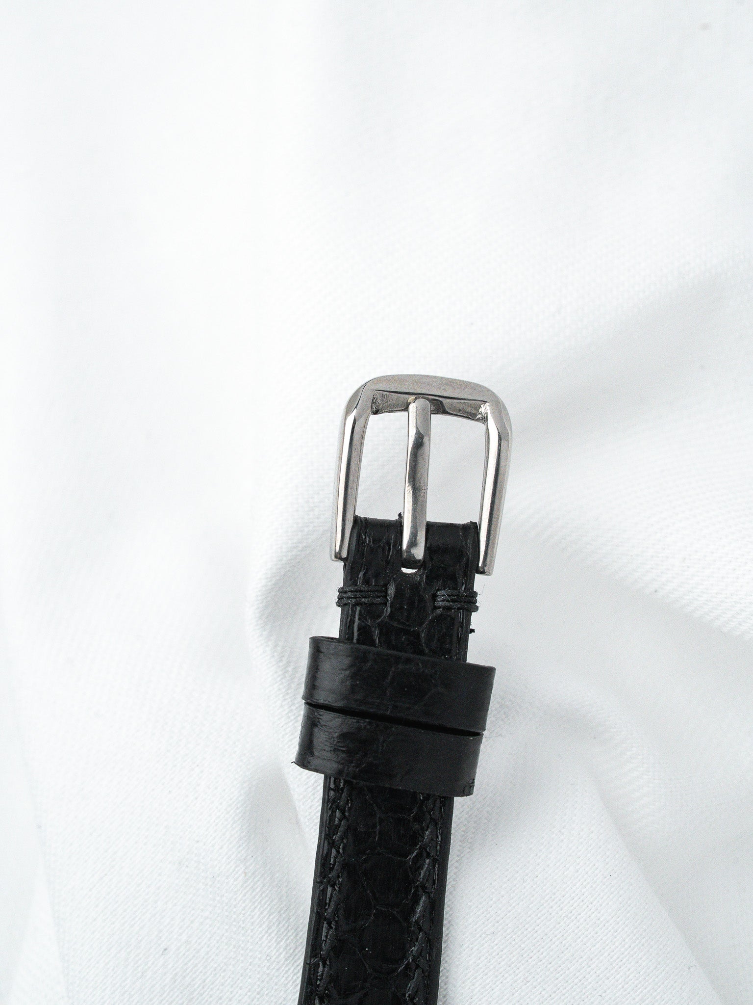 Black alligator leather watch strap with silver buckle on white background