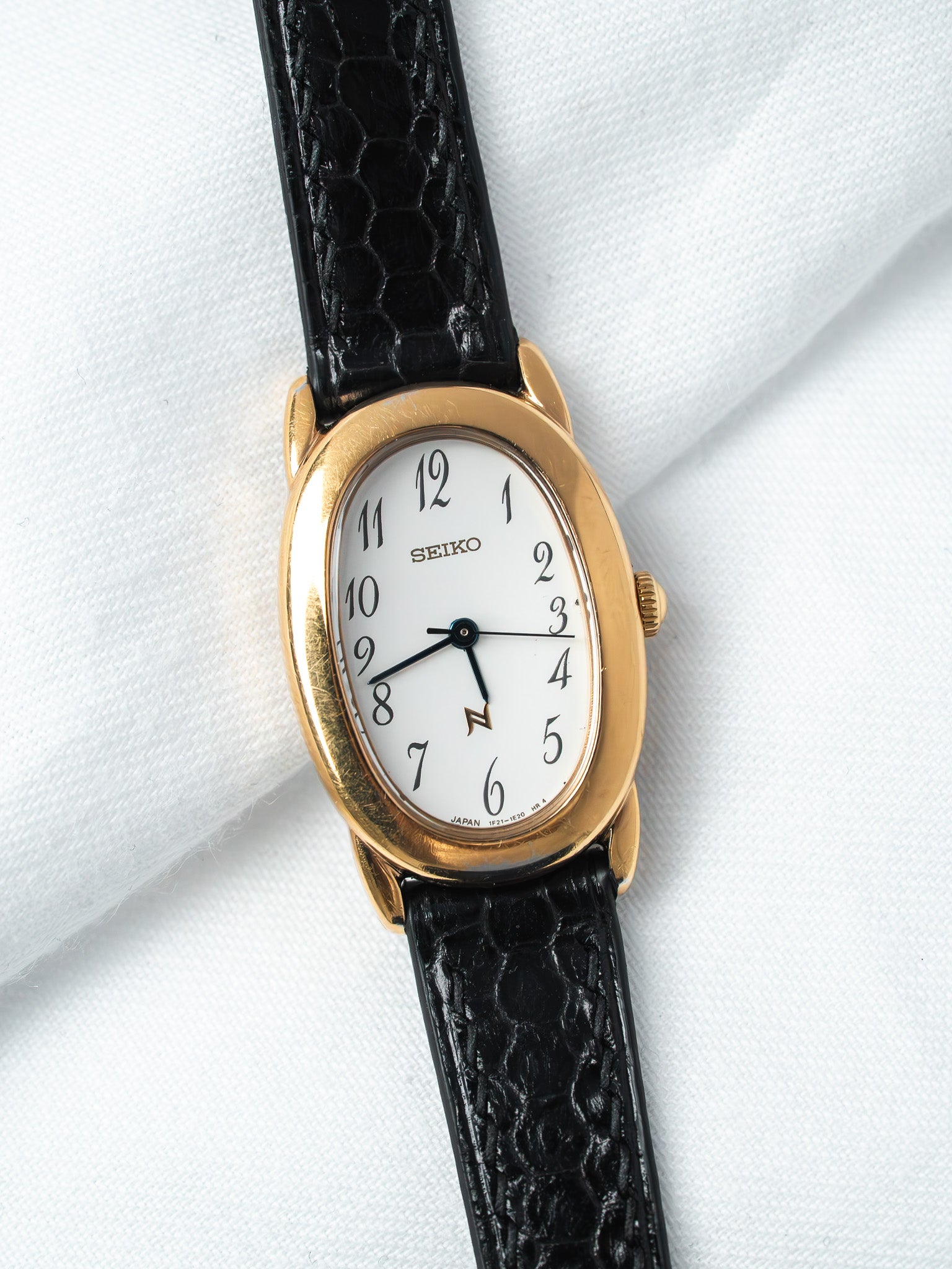 Seiko vintage watch with gold case, white dial, black crocodile strap on white fabric