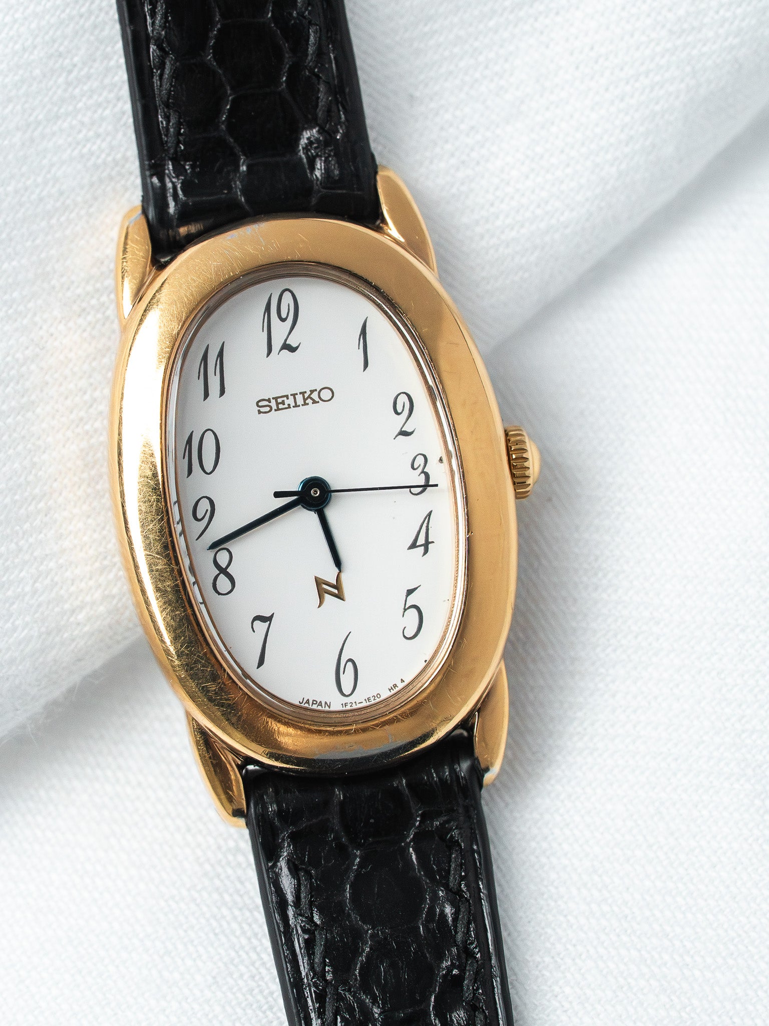Seiko vintage watch with gold case, white dial, black alligator strap on white fabric