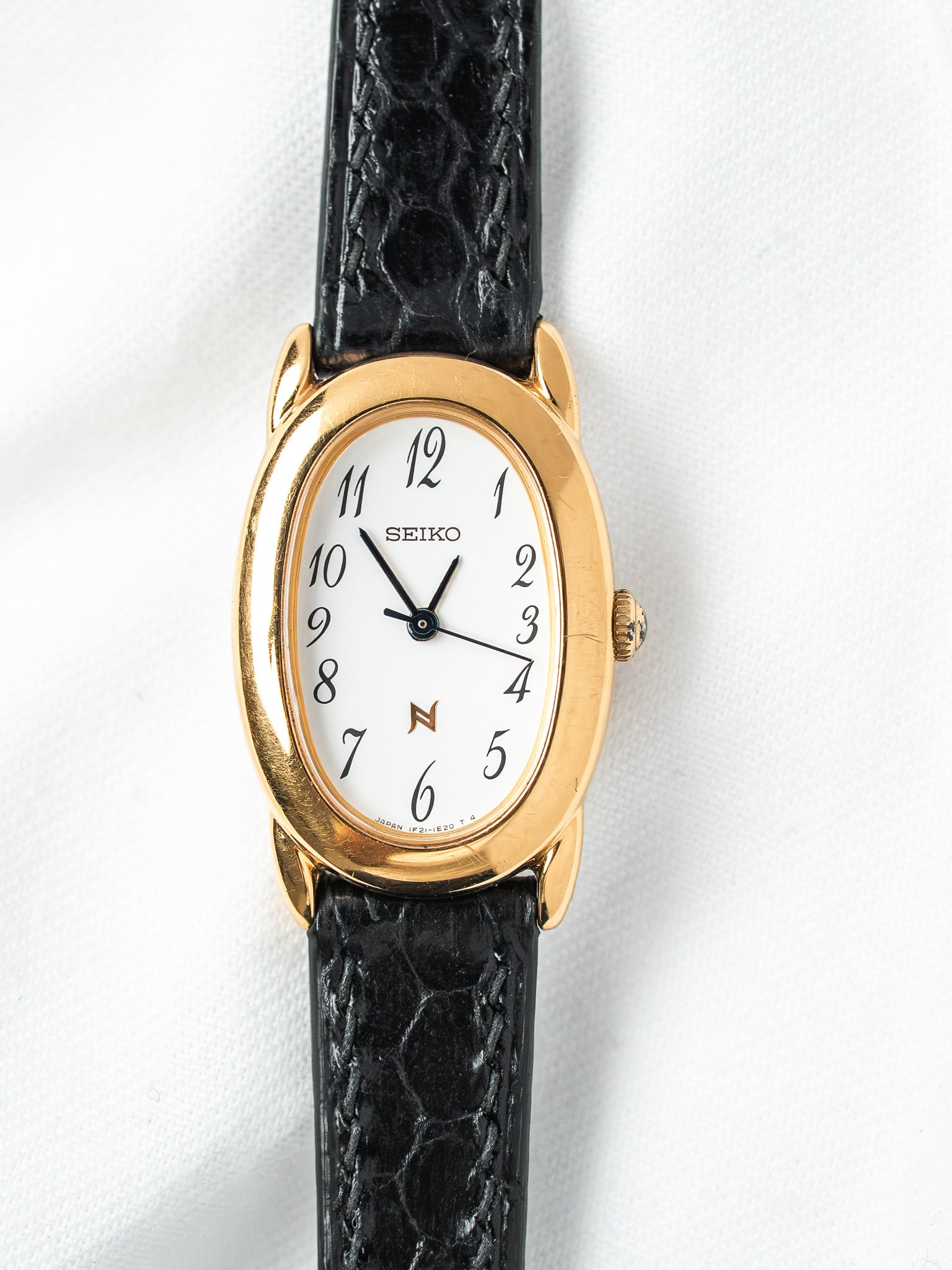 Seiko vintage watch with gold case, white dial, black alligator strap on white background
