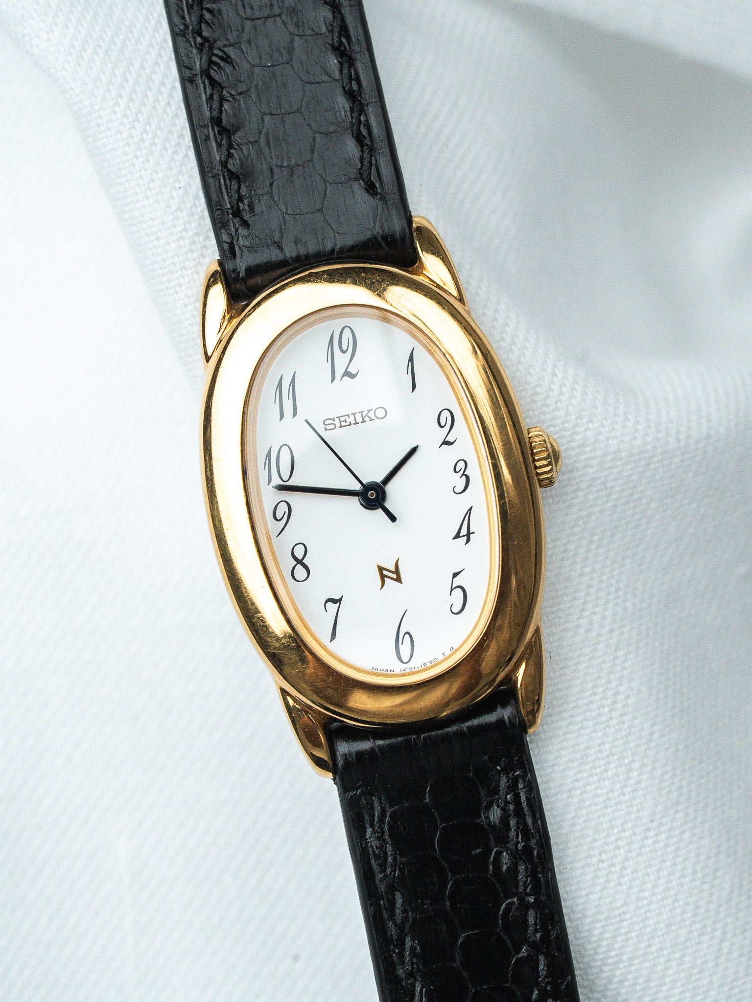 Seiko vintage watch with gold case, white dial, black alligator strap on white fabric