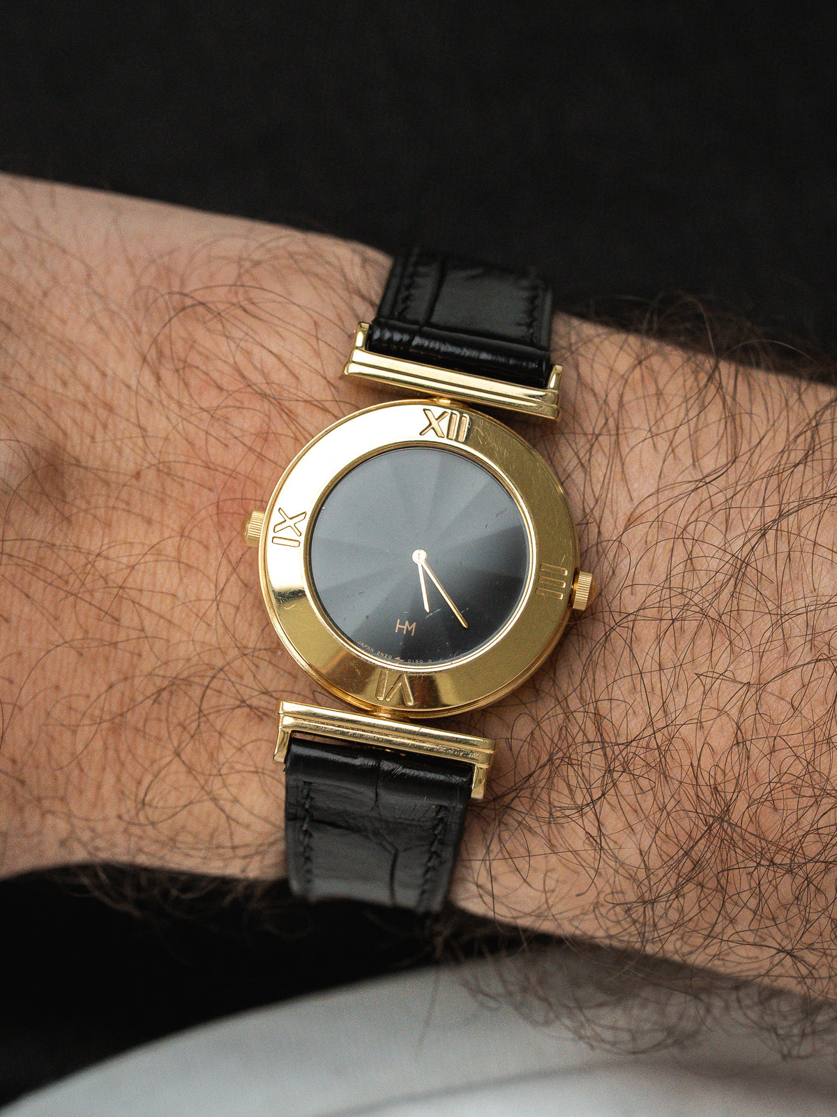 Vintage HM watch with gold case, black dial, Roman numerals, and black leather strap on wrist
