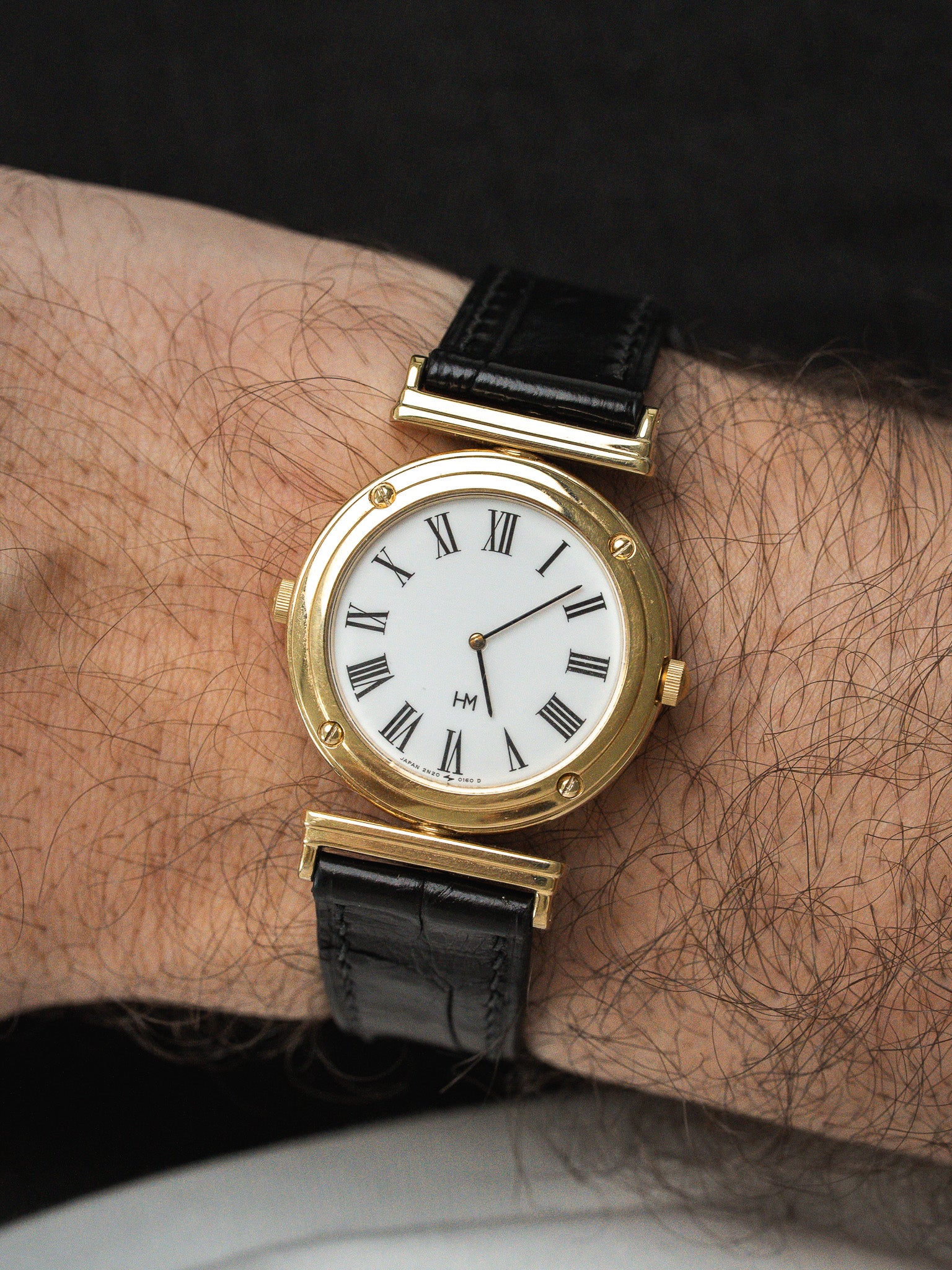 Montre HM vintage en or jaune, cadran blanc chiffres romains, bracelet cuir noir portée au poignet