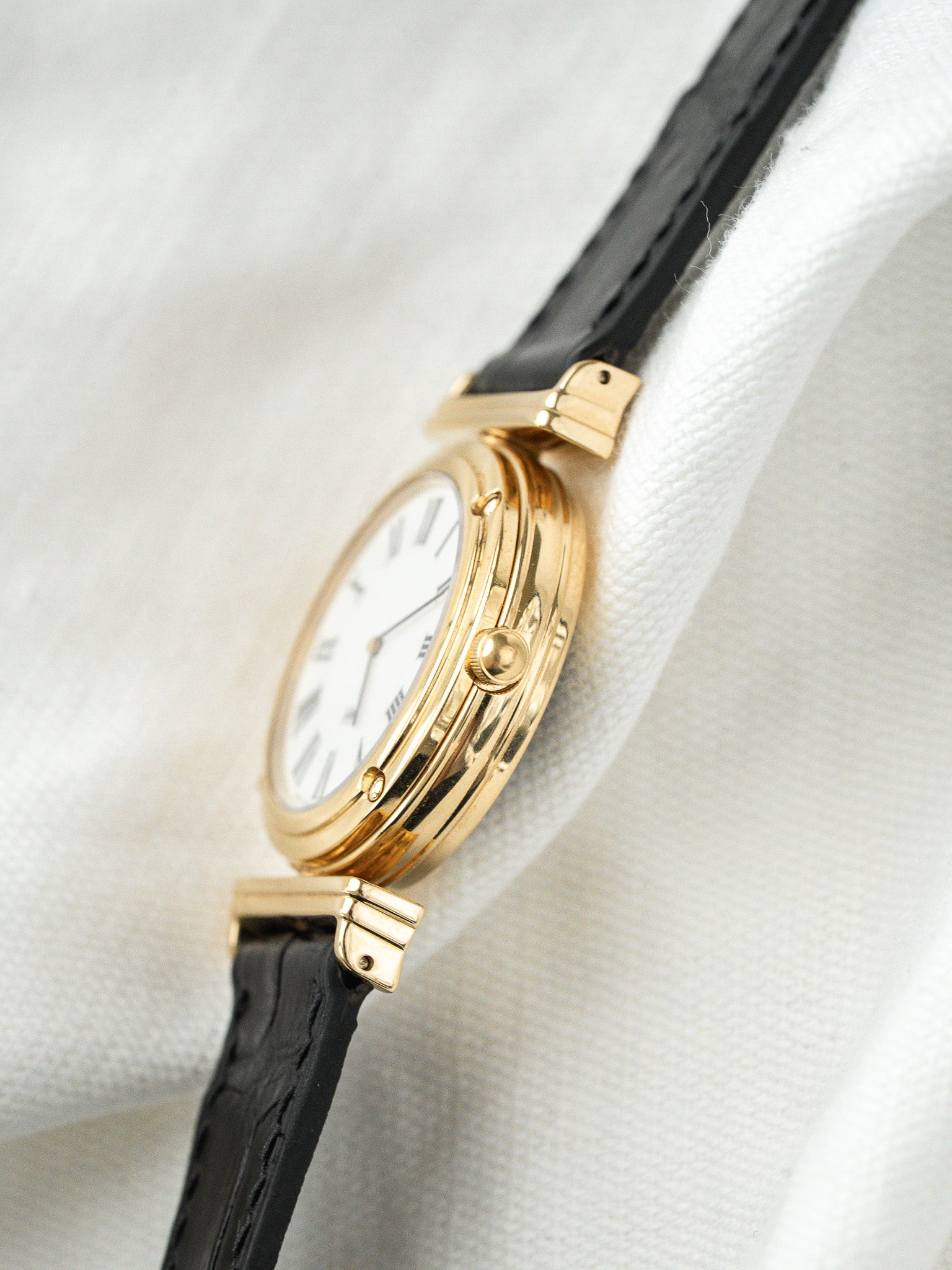 Cartier vintage watch with gold case, white dial, black leather strap on fabric