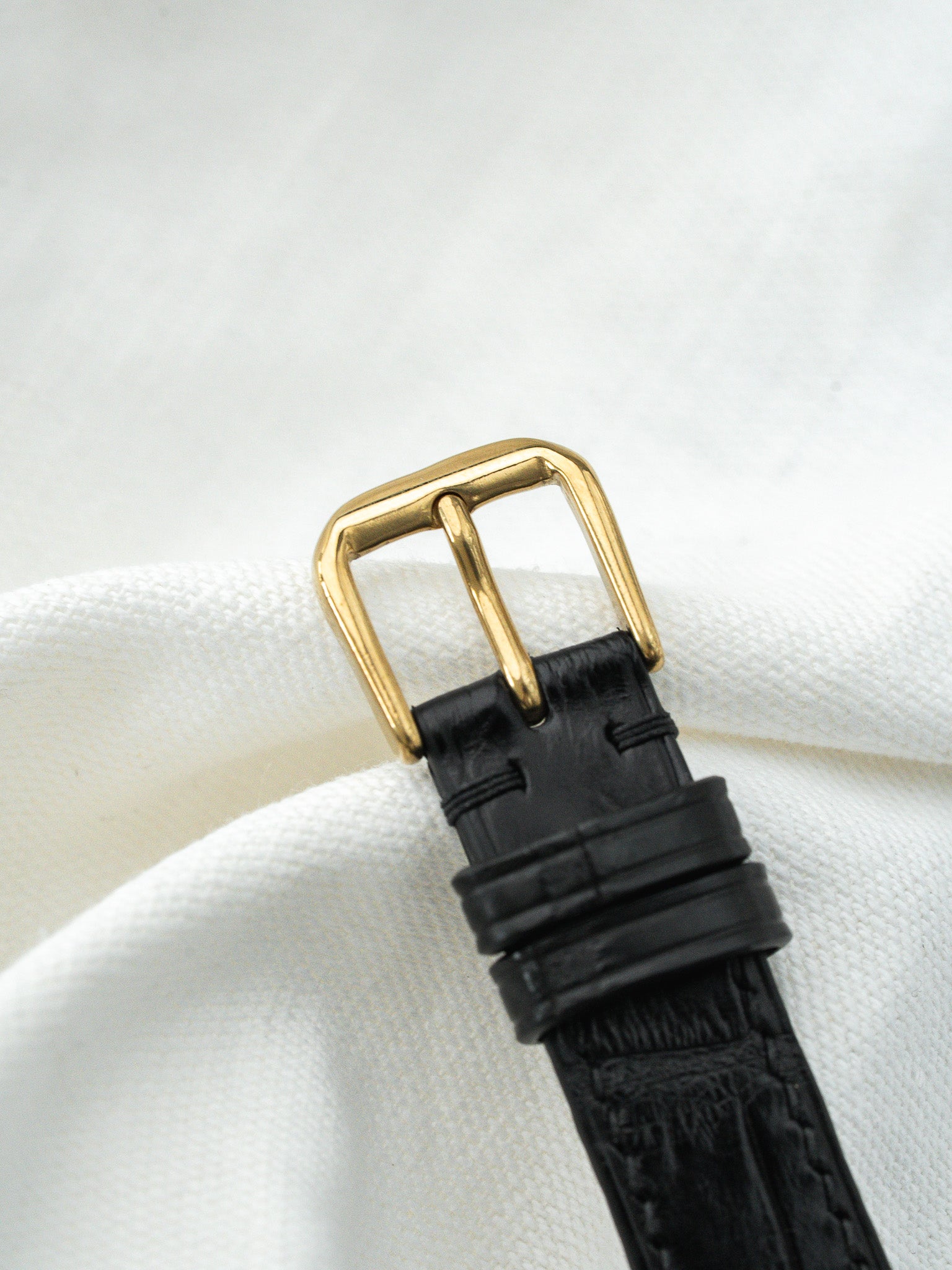 Black alligator leather watch strap with gold buckle on white fabric