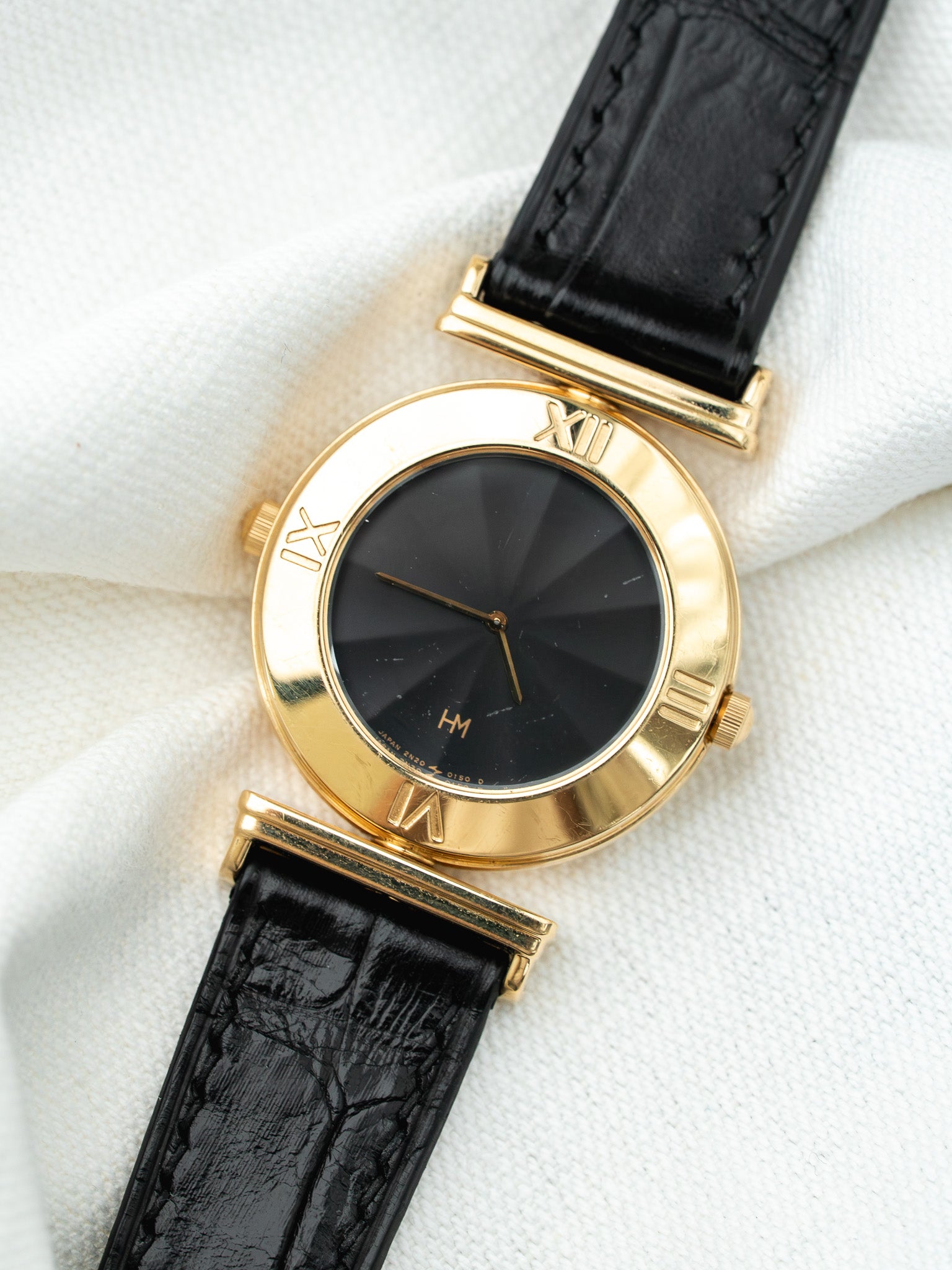 Montre HM vintage en or jaune, cadran noir rayonnant, bracelet cuir noir