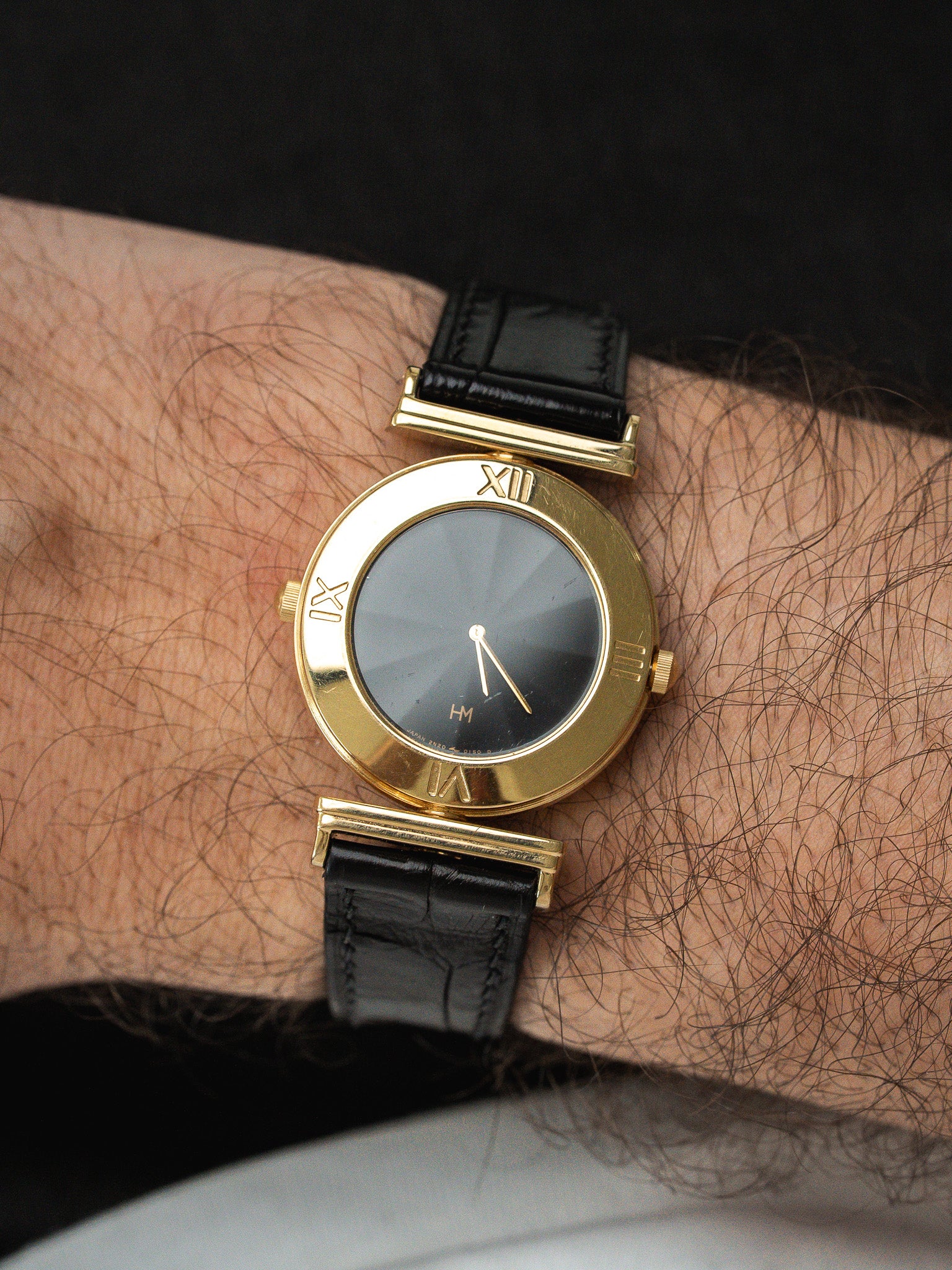 Vintage HM watch with gold case, black dial, Roman numerals, and black leather strap on wrist
