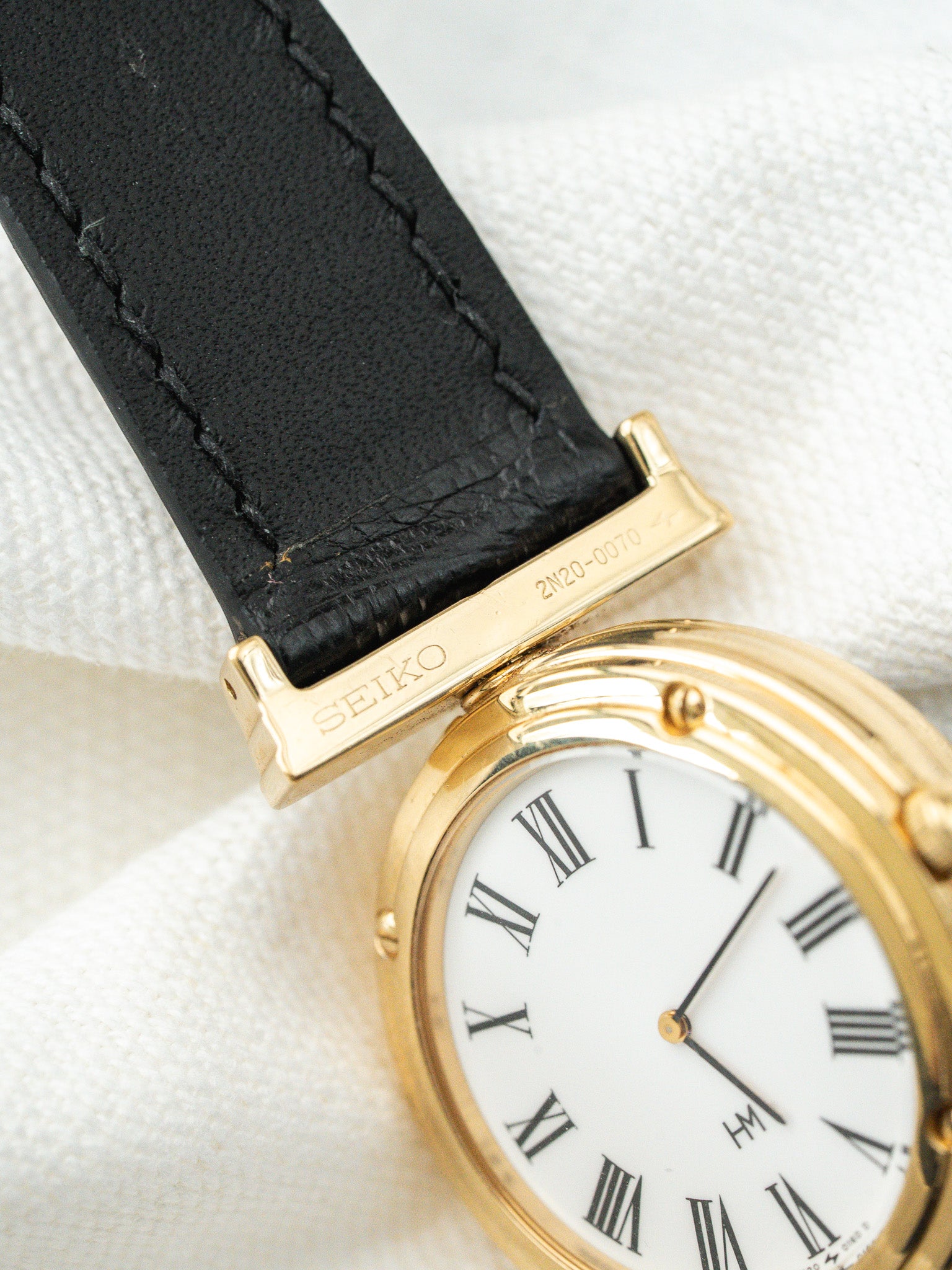 Seiko vintage watch with gold case, white dial, Roman numerals, black leather strap
