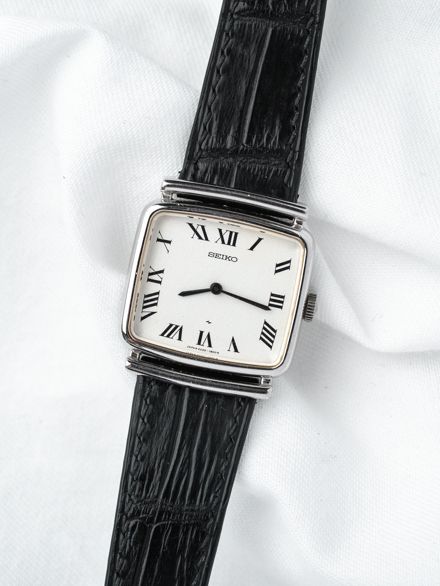 Seiko vintage watch with white dial, Roman numerals, black leather strap on white fabric