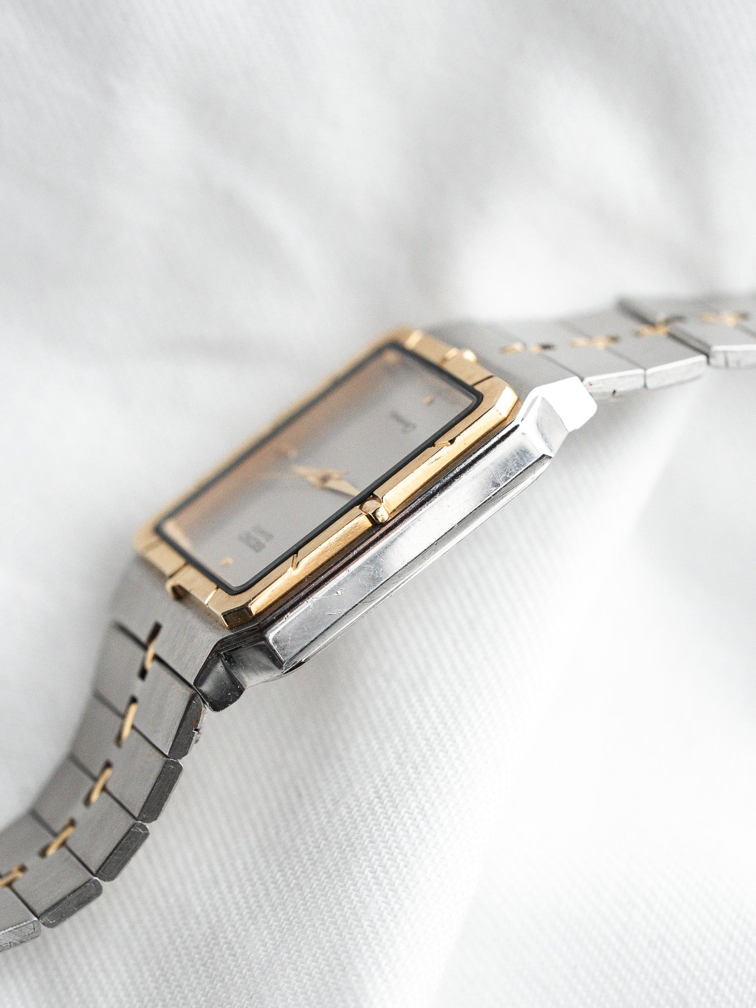 Vintage Cartier watch with gold bezel, silver case, and metal bracelet on white fabric