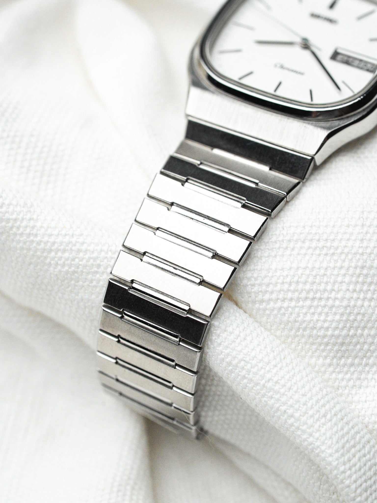 Omega vintage watch with white dial, steel bracelet, resting on white fabric
