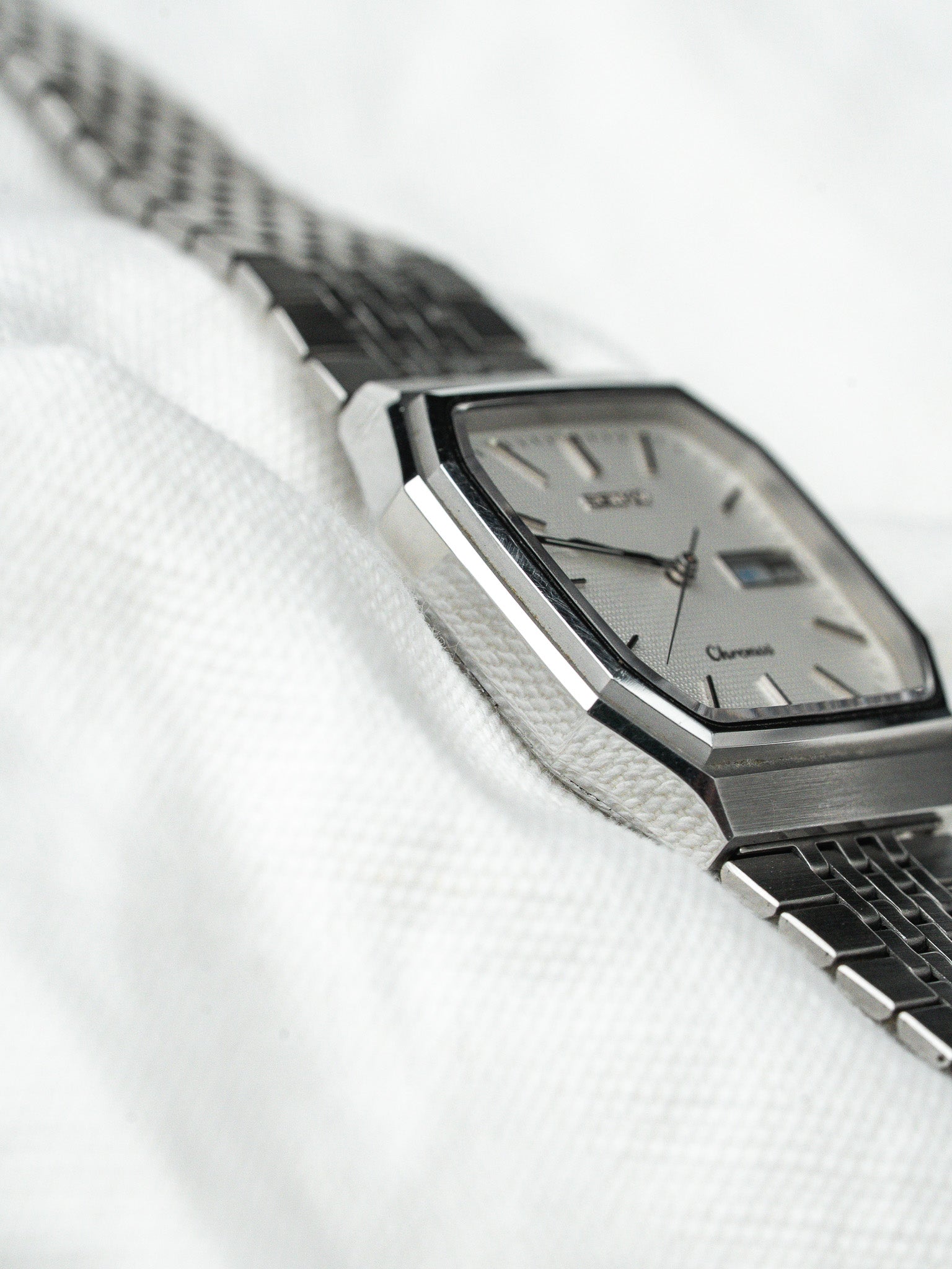 Vintage Doxa Chronos watch with silver dial, octagonal case, and metal bracelet on white fabric